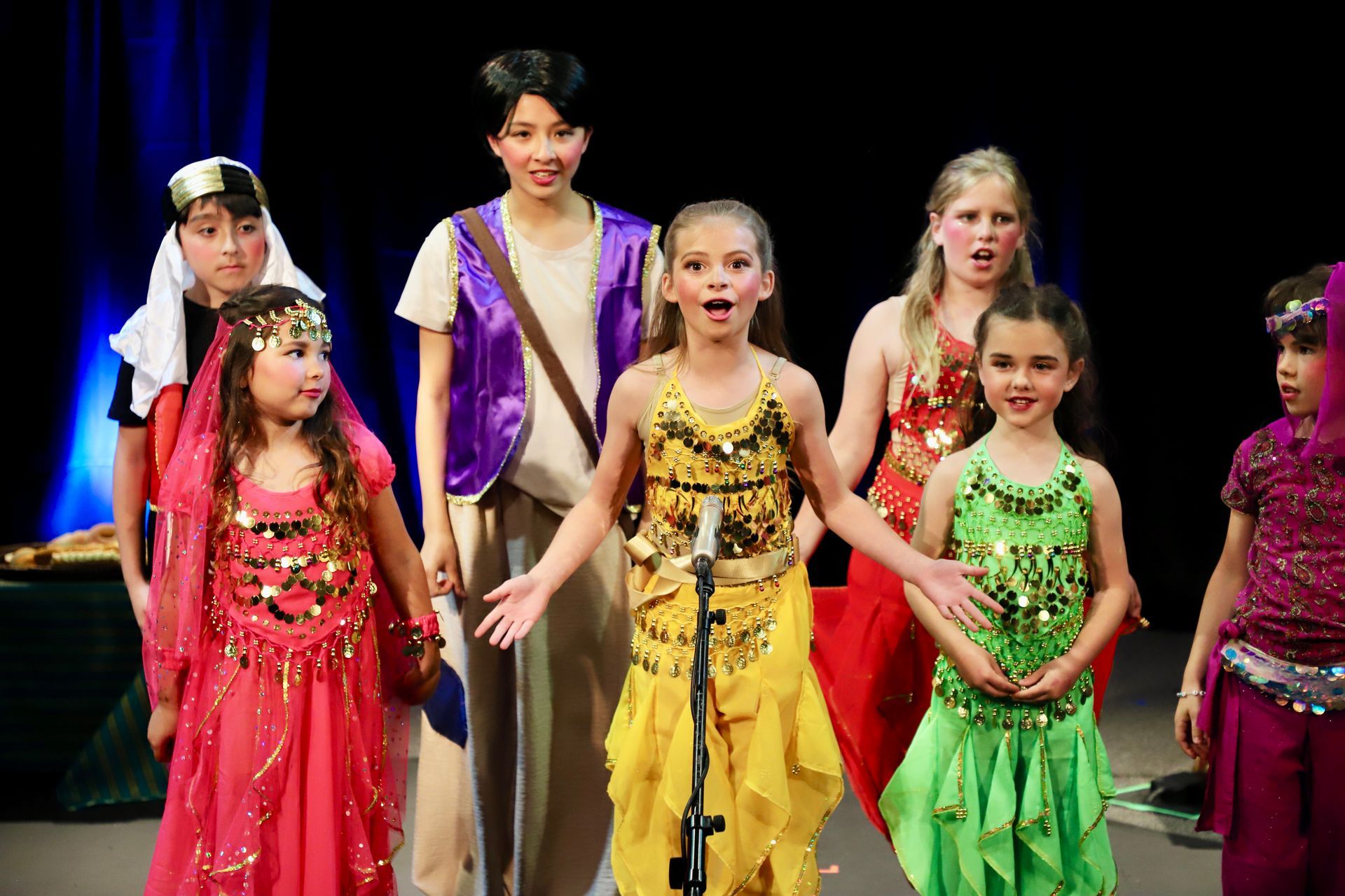 A group of children are singing into a microphone on a stage.