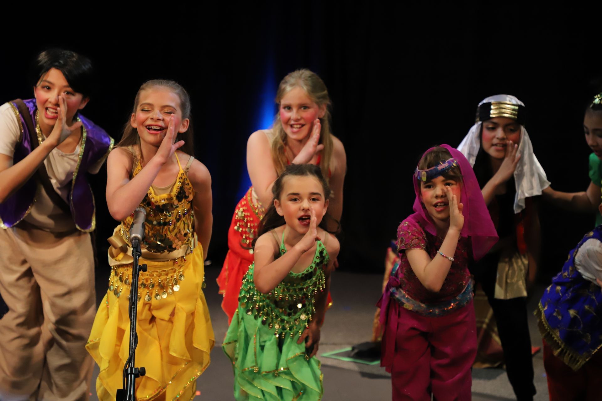 A group of young girls in costume are standing in front of a microphone on a stage.