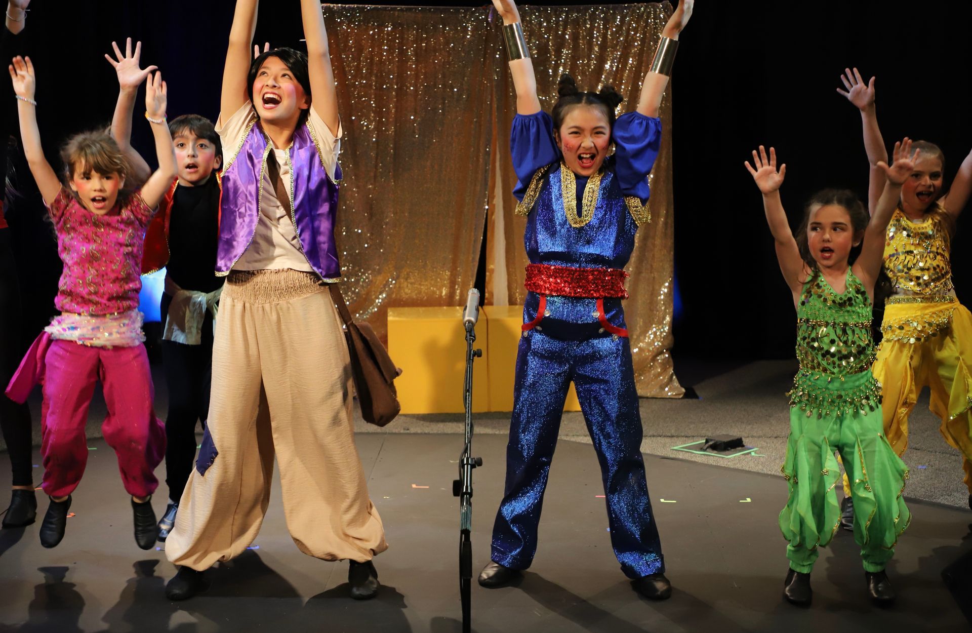 A group of children are dancing on a stage with their arms in the air