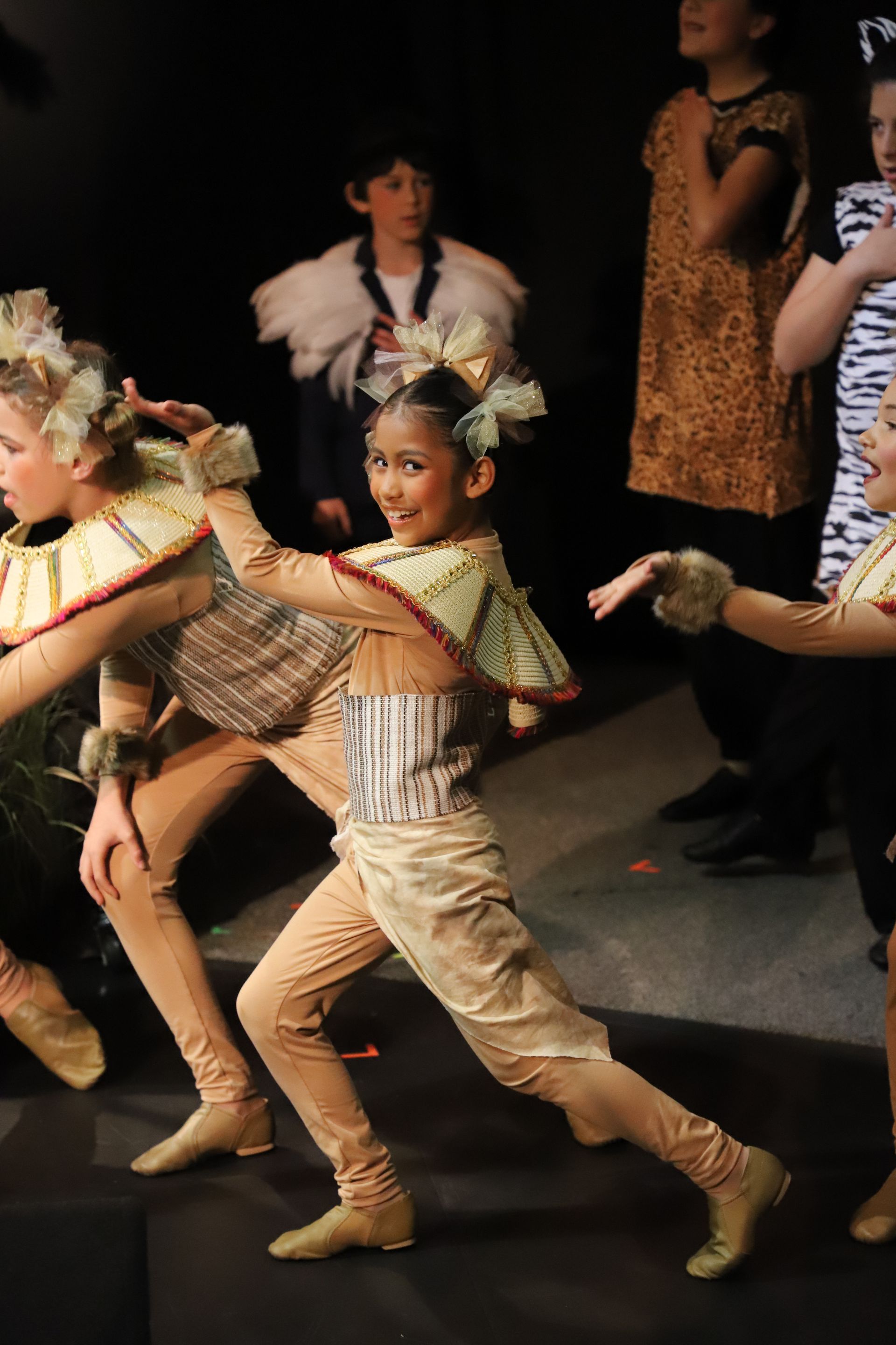 A group of young girls in costume are dancing on a stage.