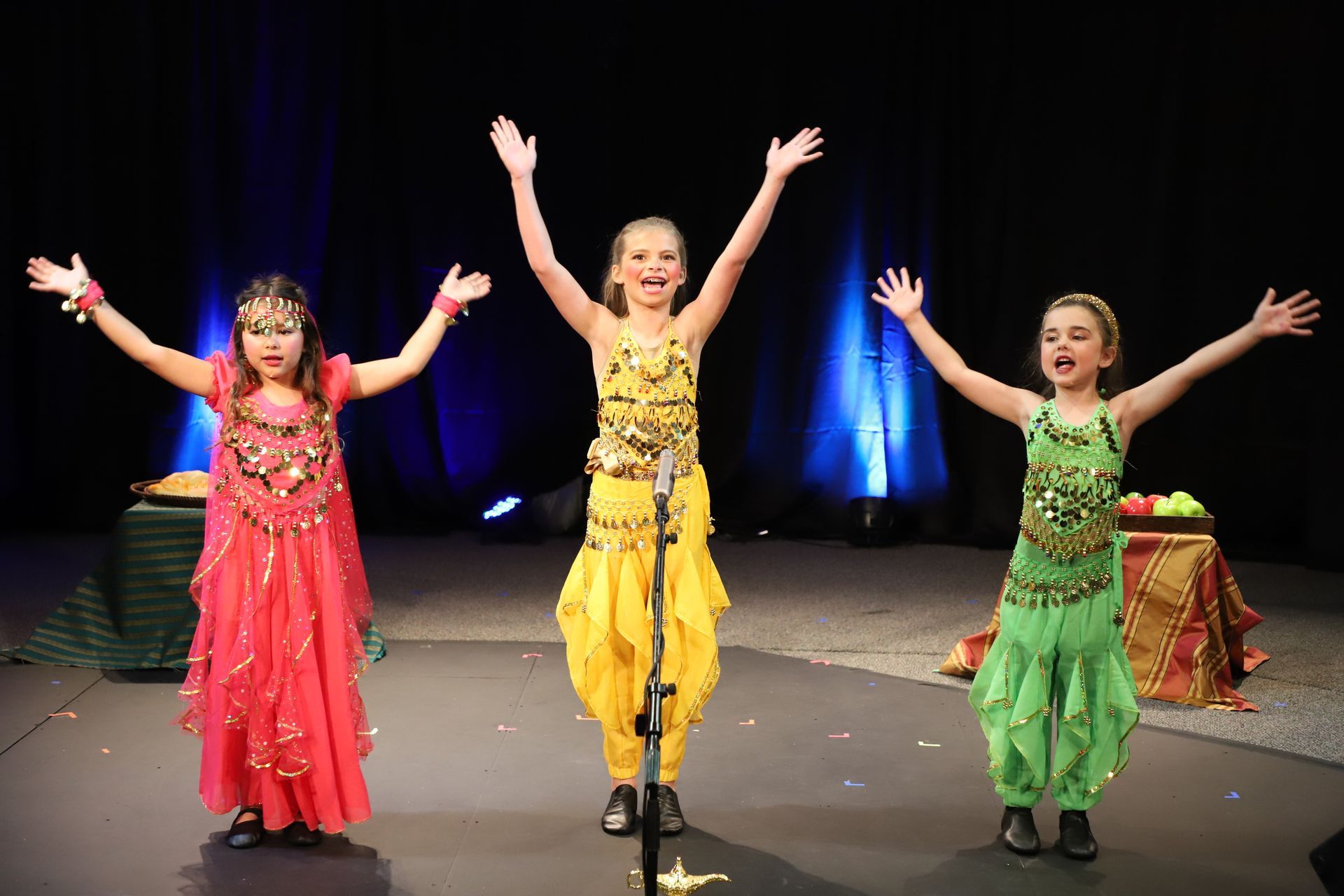 Three young girls are dancing on a stage with their arms in the air.