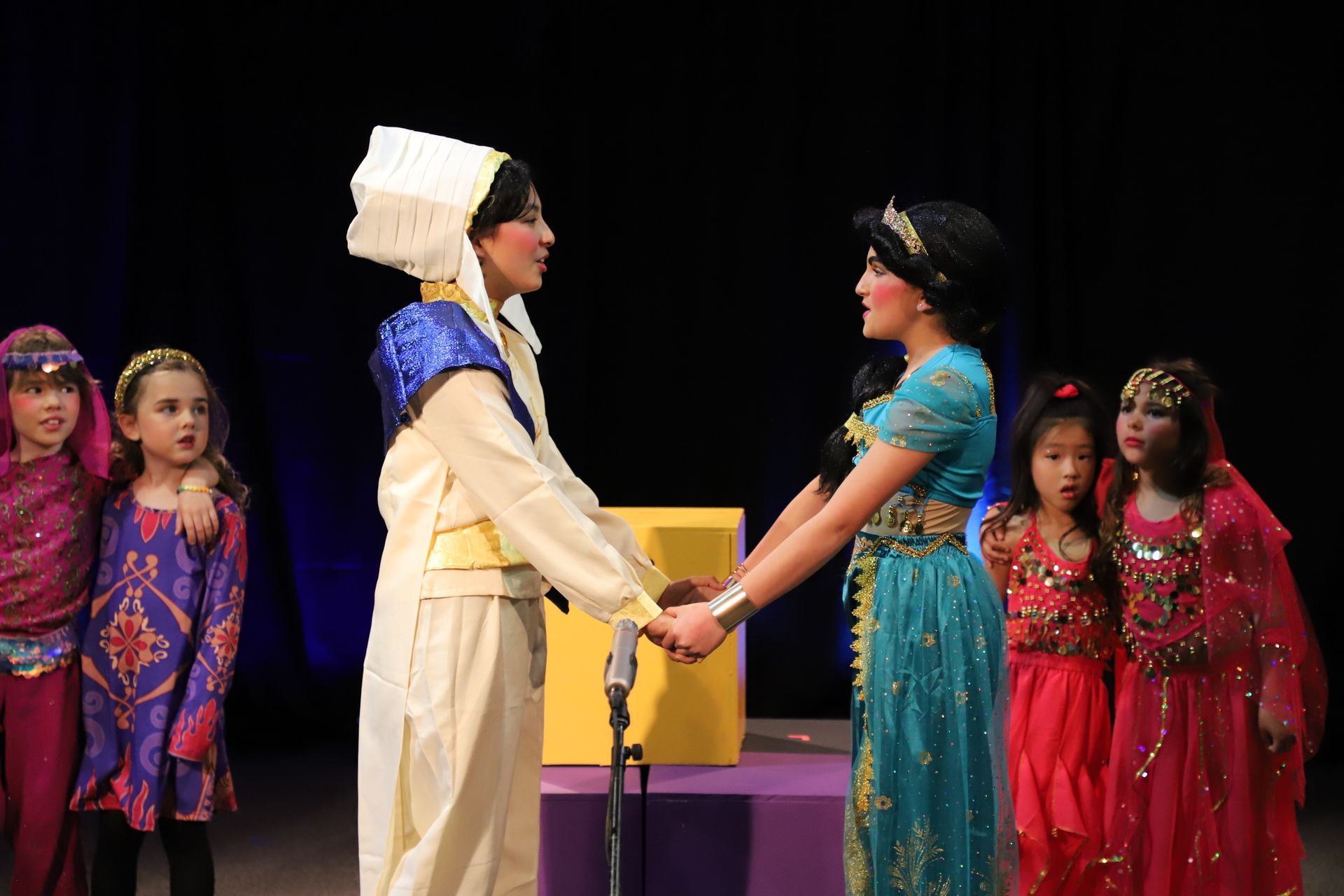 A group of children in costume are holding hands on a stage.