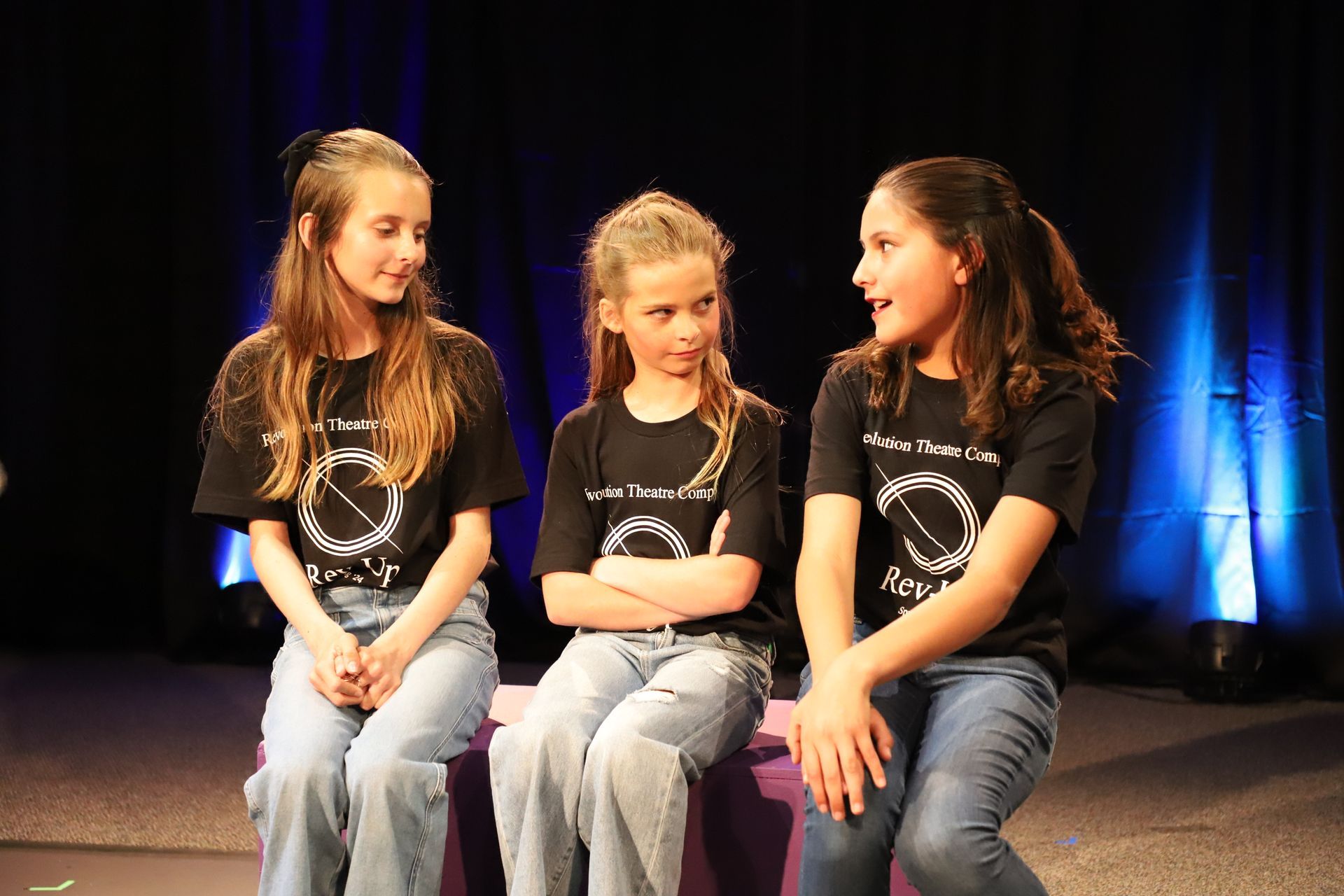 Three young girls are sitting next to each other on a stage.