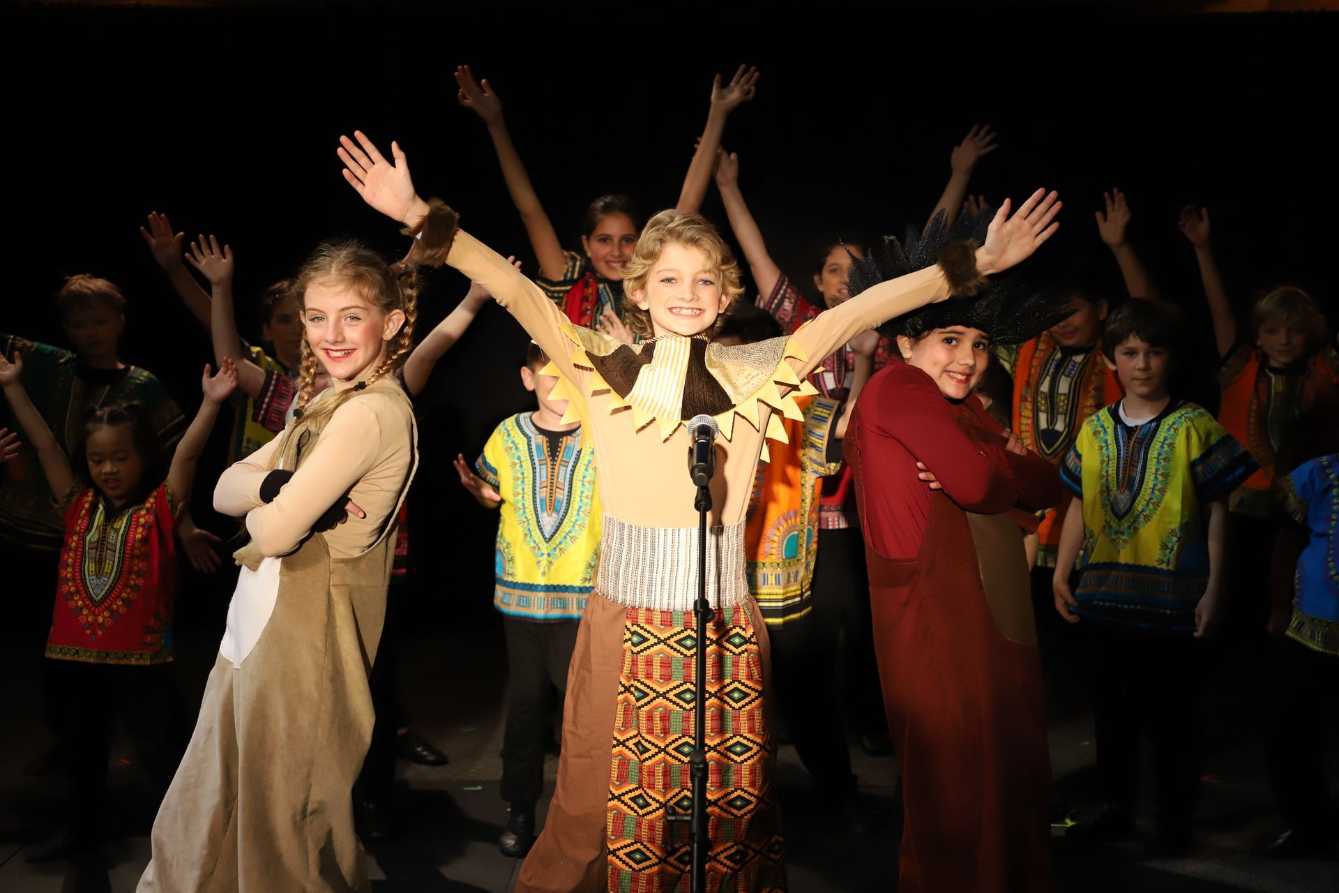 A group of children are singing into a microphone on a stage.