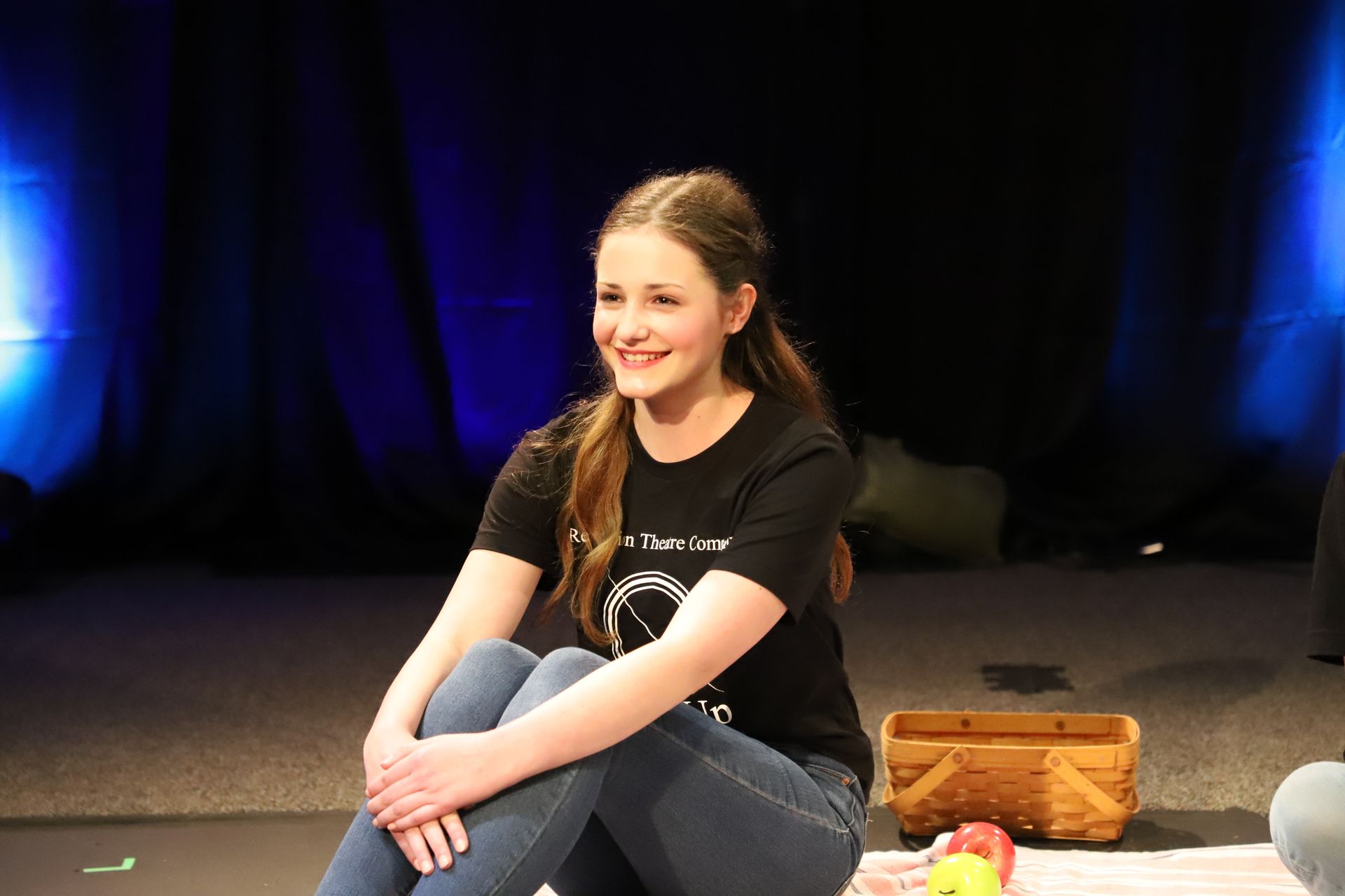 A young girl is sitting on a blanket on a stage.
