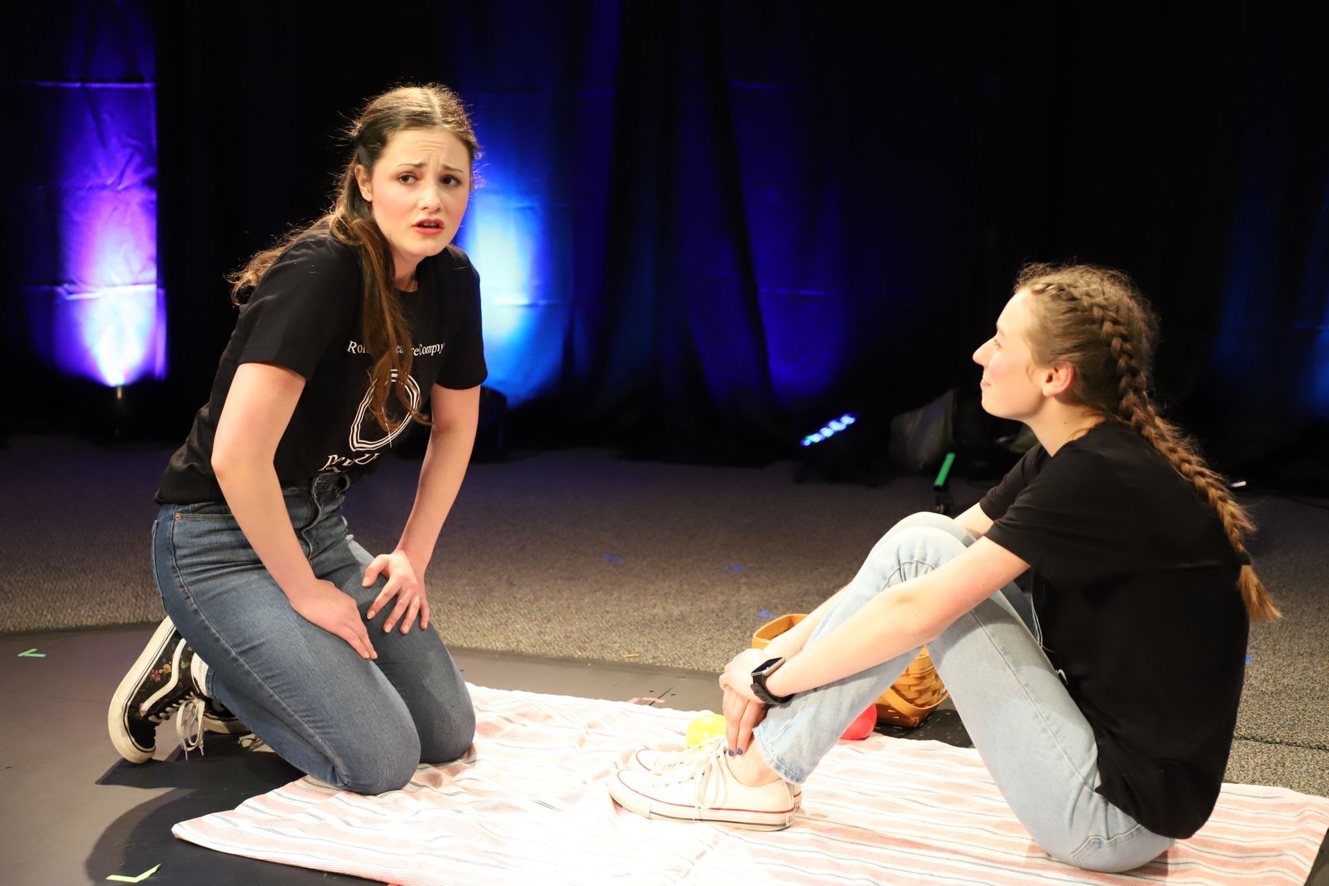 Two young women are sitting on a blanket on a stage.