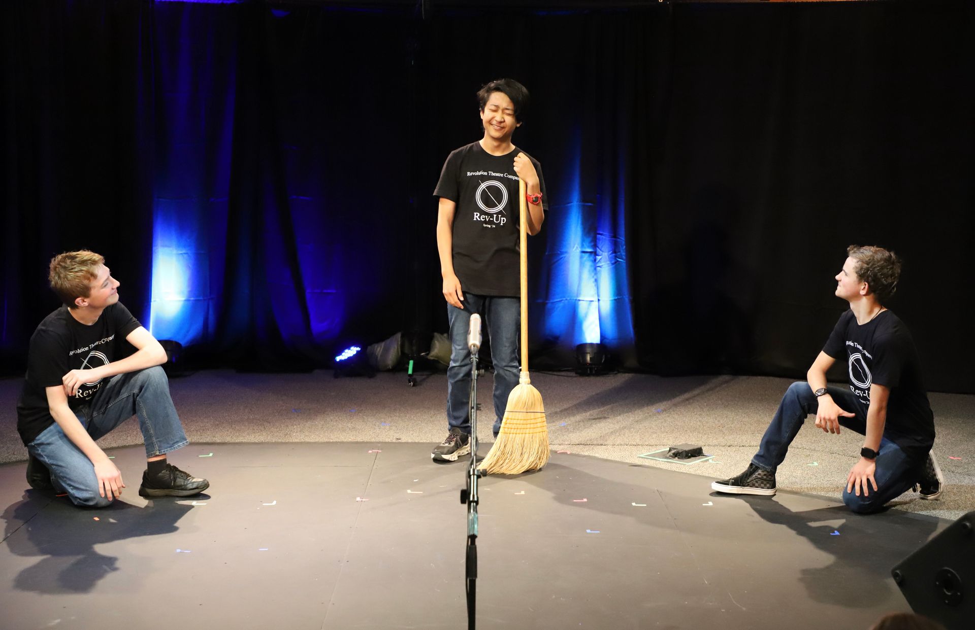 A man is standing in front of a microphone holding a broom.