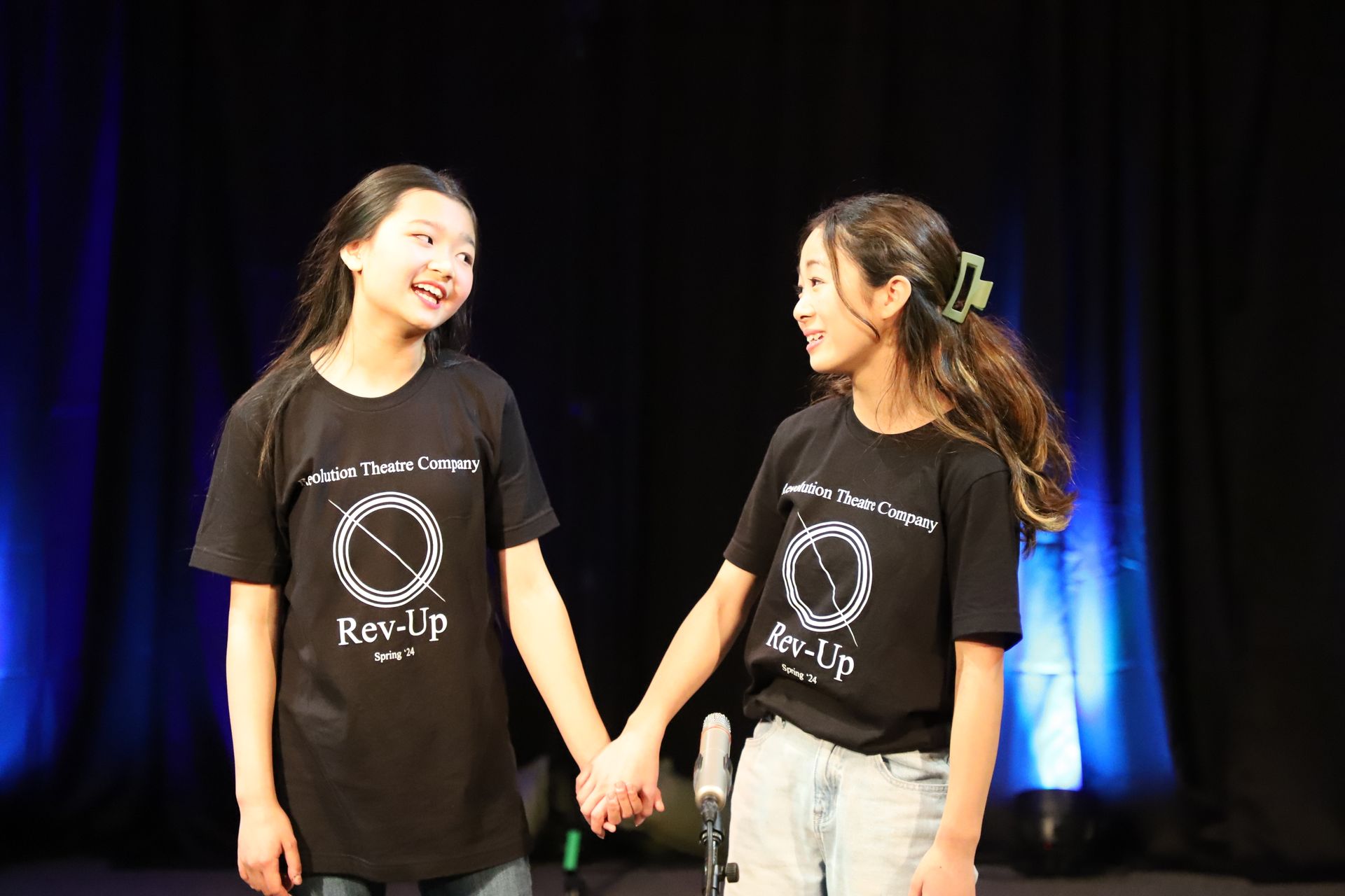 Two young girls are holding hands on a stage.