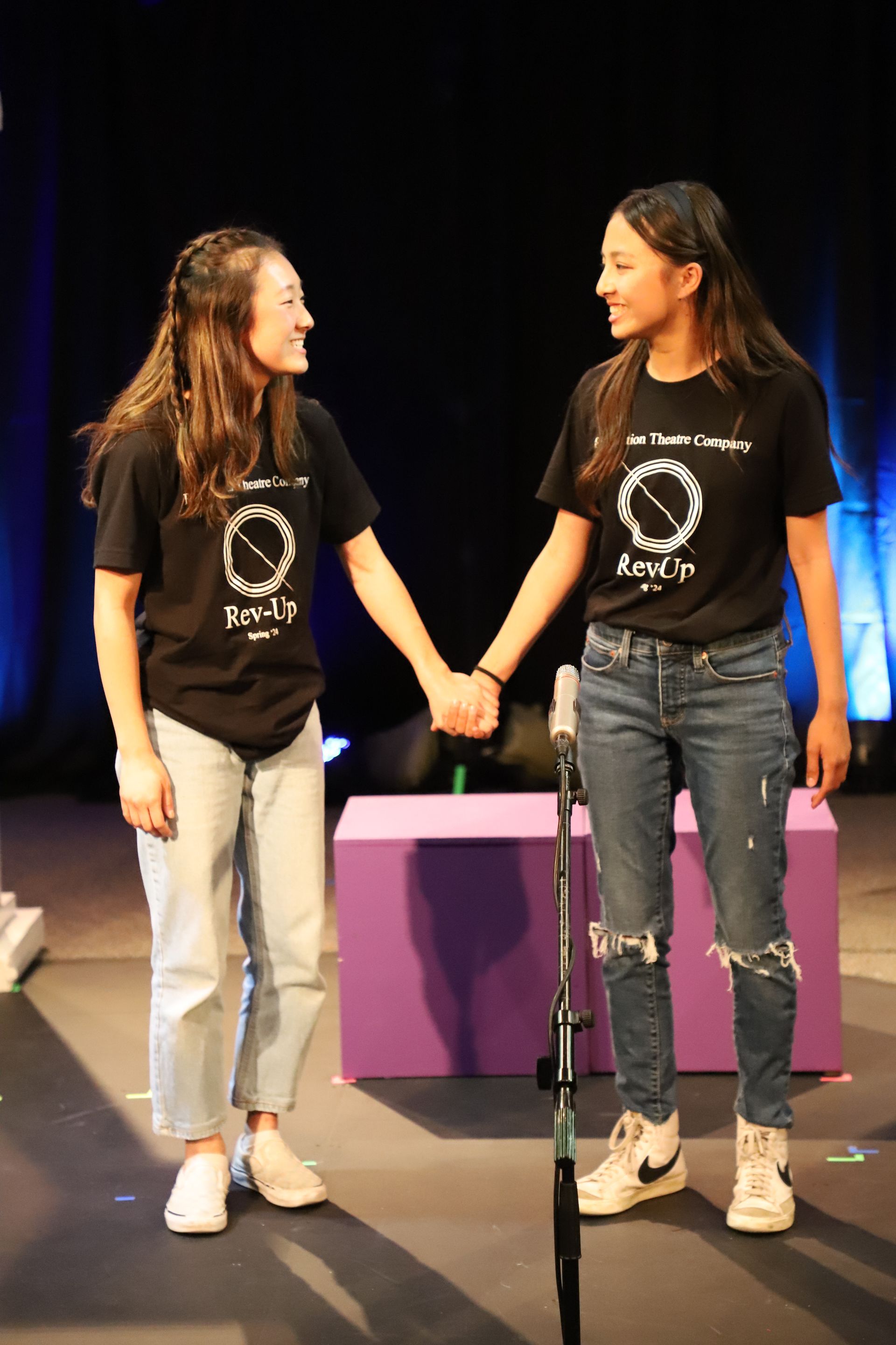 Two women are holding hands on a stage in front of a microphone.