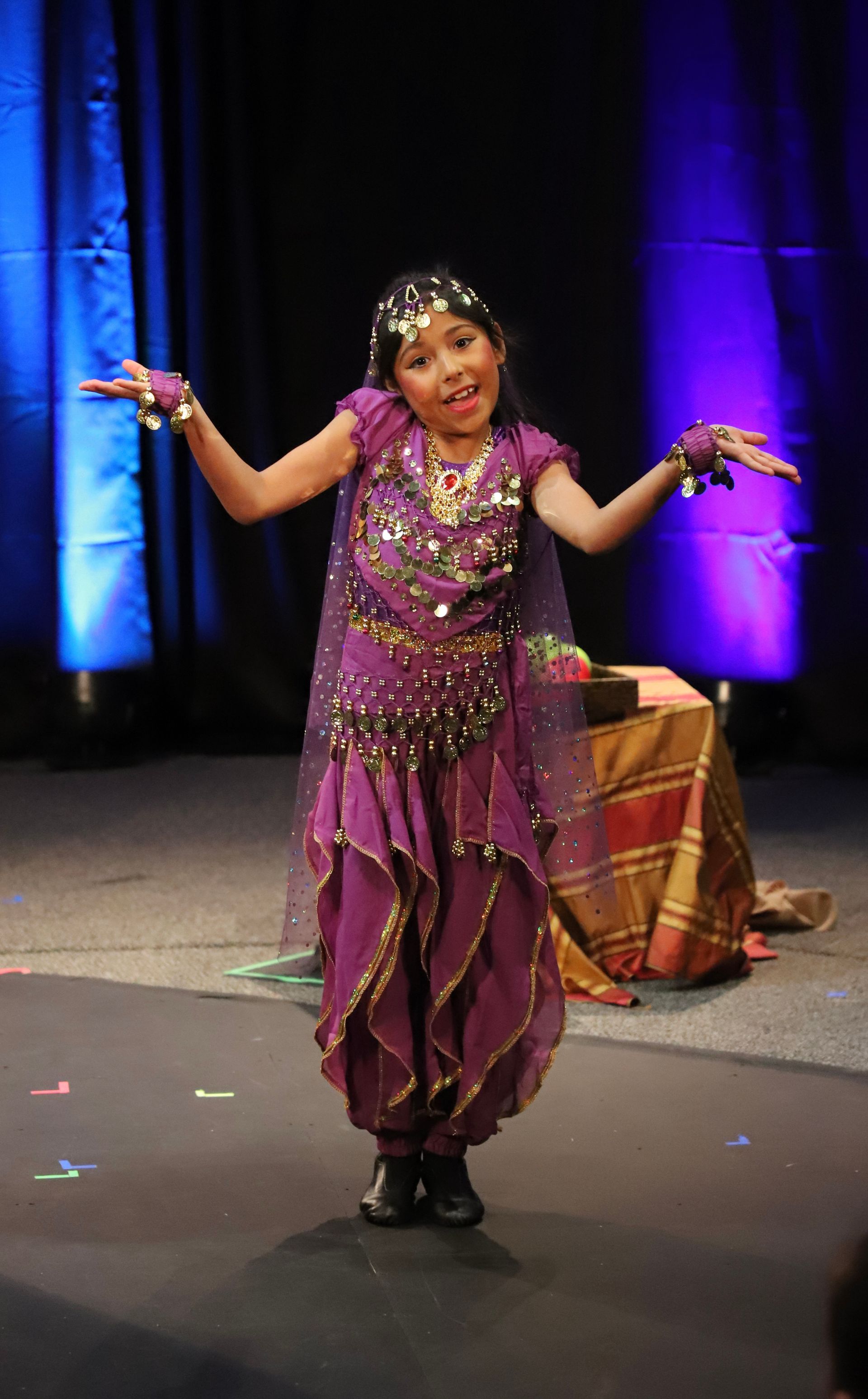 A little girl in a purple dress is dancing on a stage.