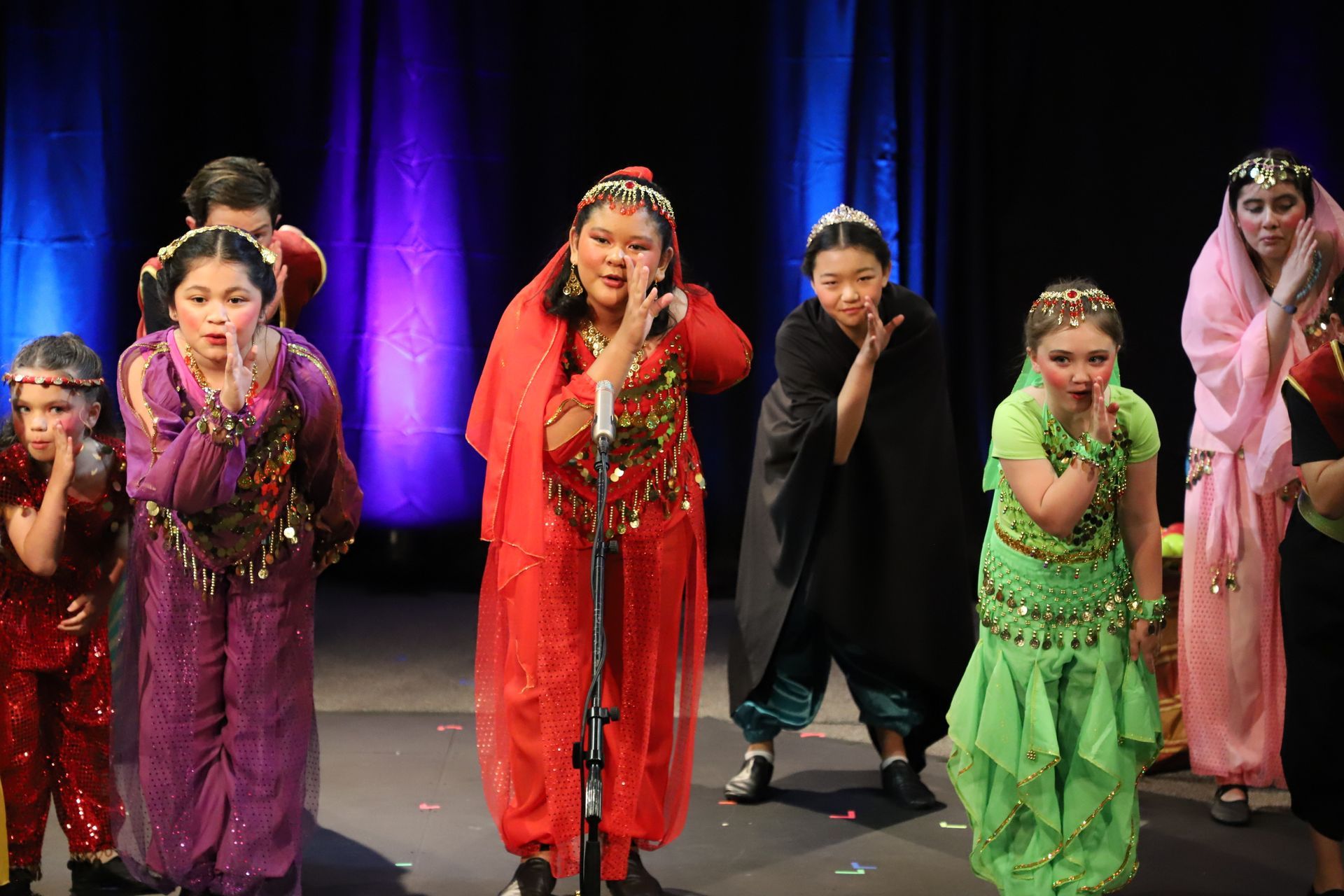 A group of children are dancing on a stage in front of a microphone.