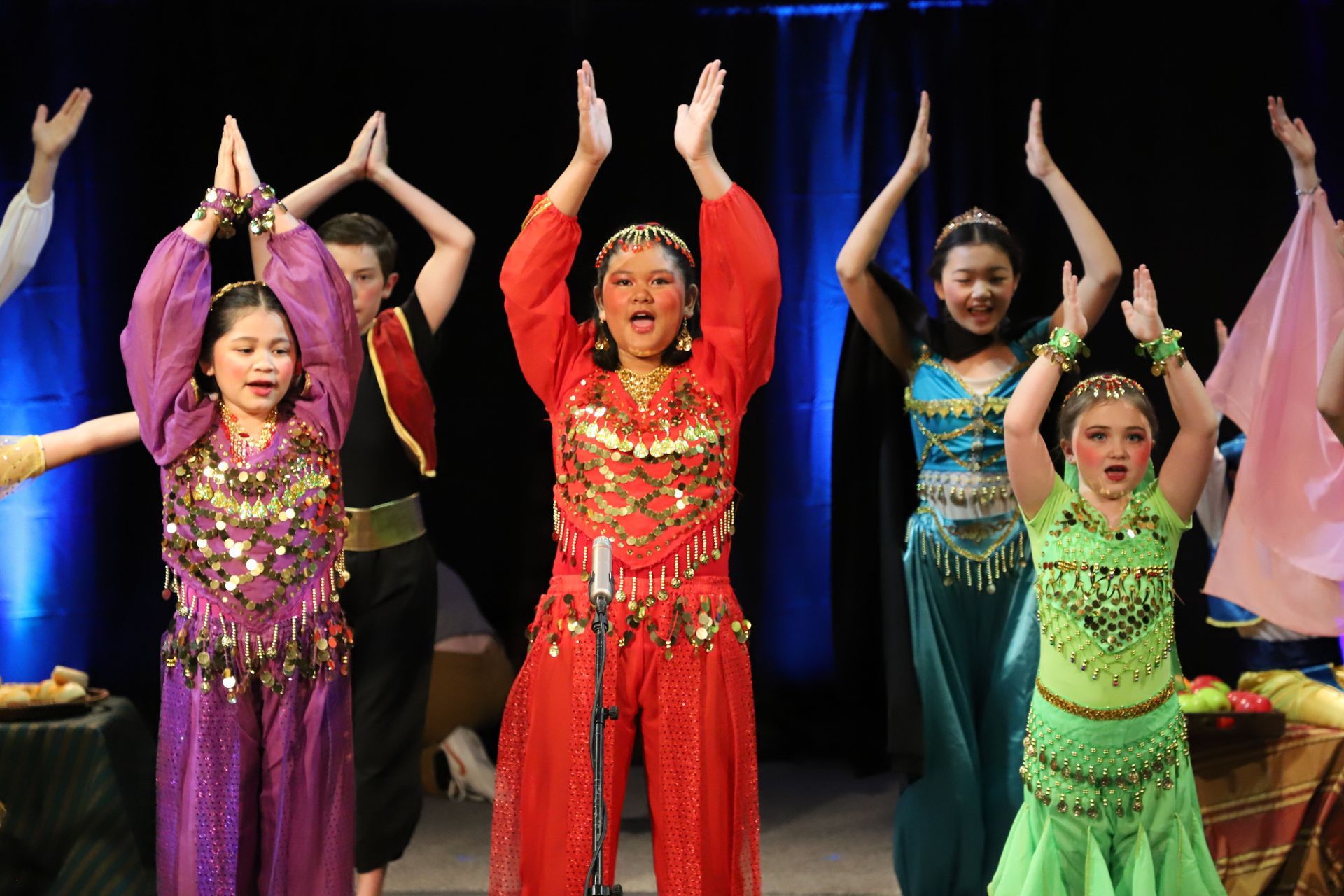 A group of children are dancing on a stage with their hands in the air.
