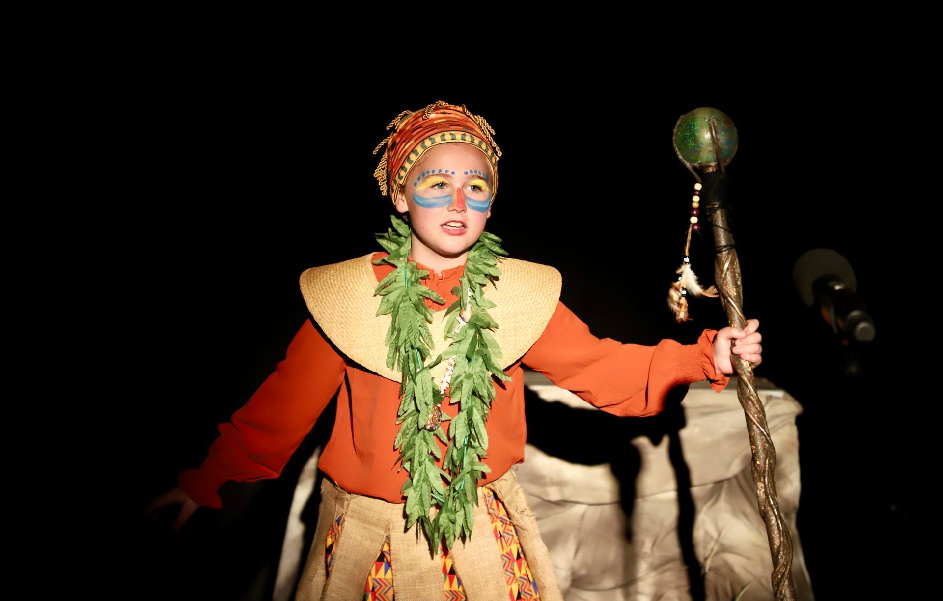 A young boy in a costume is holding a cane in the dark.