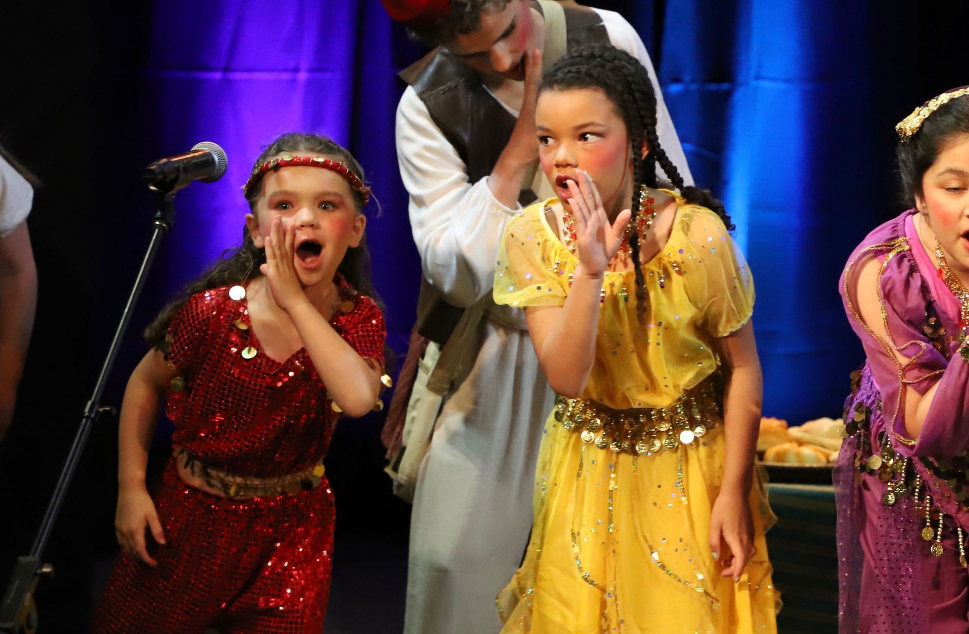 A group of young girls are standing on a stage in front of a microphone.