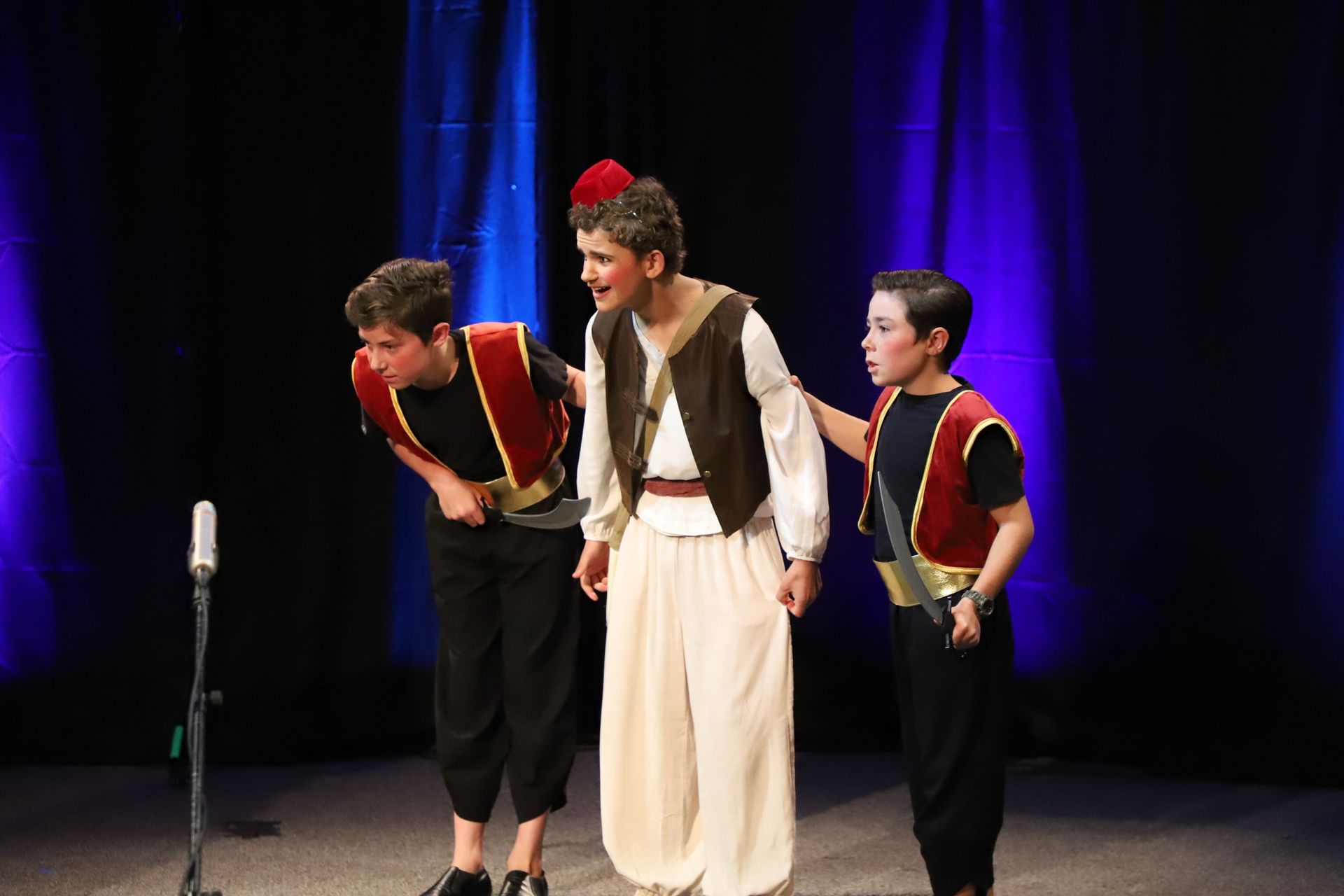 Three young boys are standing next to each other on a stage in front of a microphone.