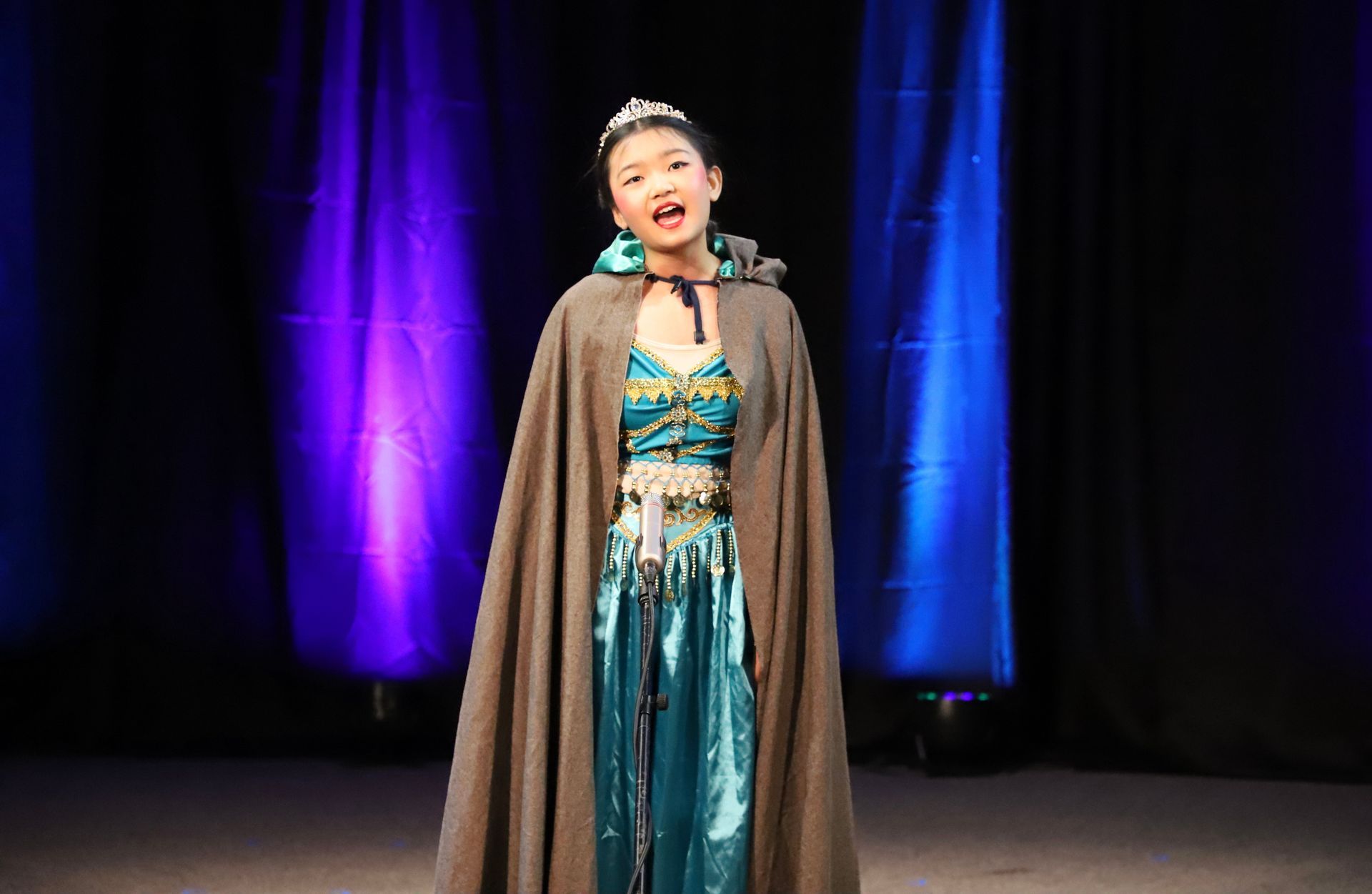A young girl in a costume is singing on a stage.