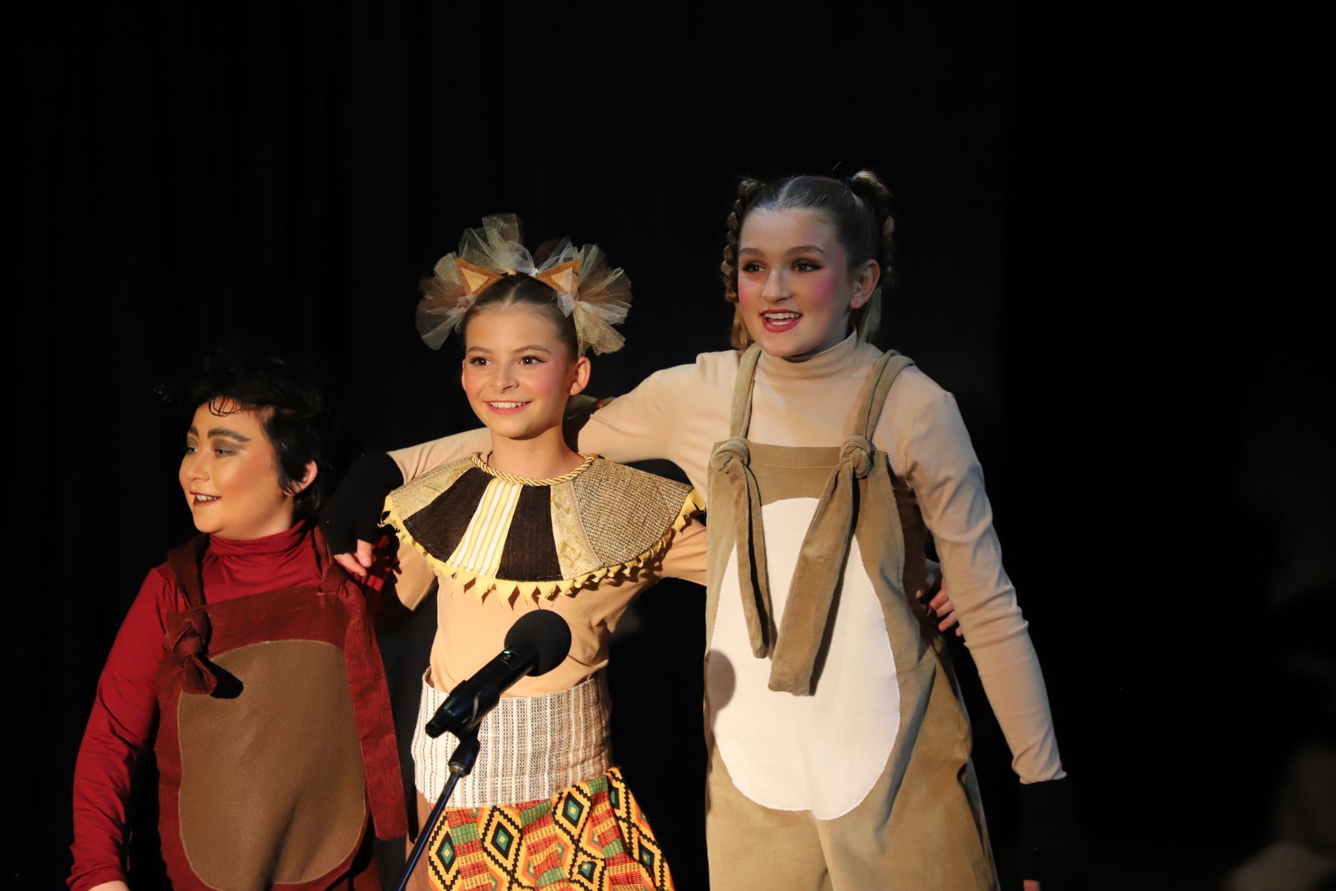 Three young girls are standing next to each other on a stage.