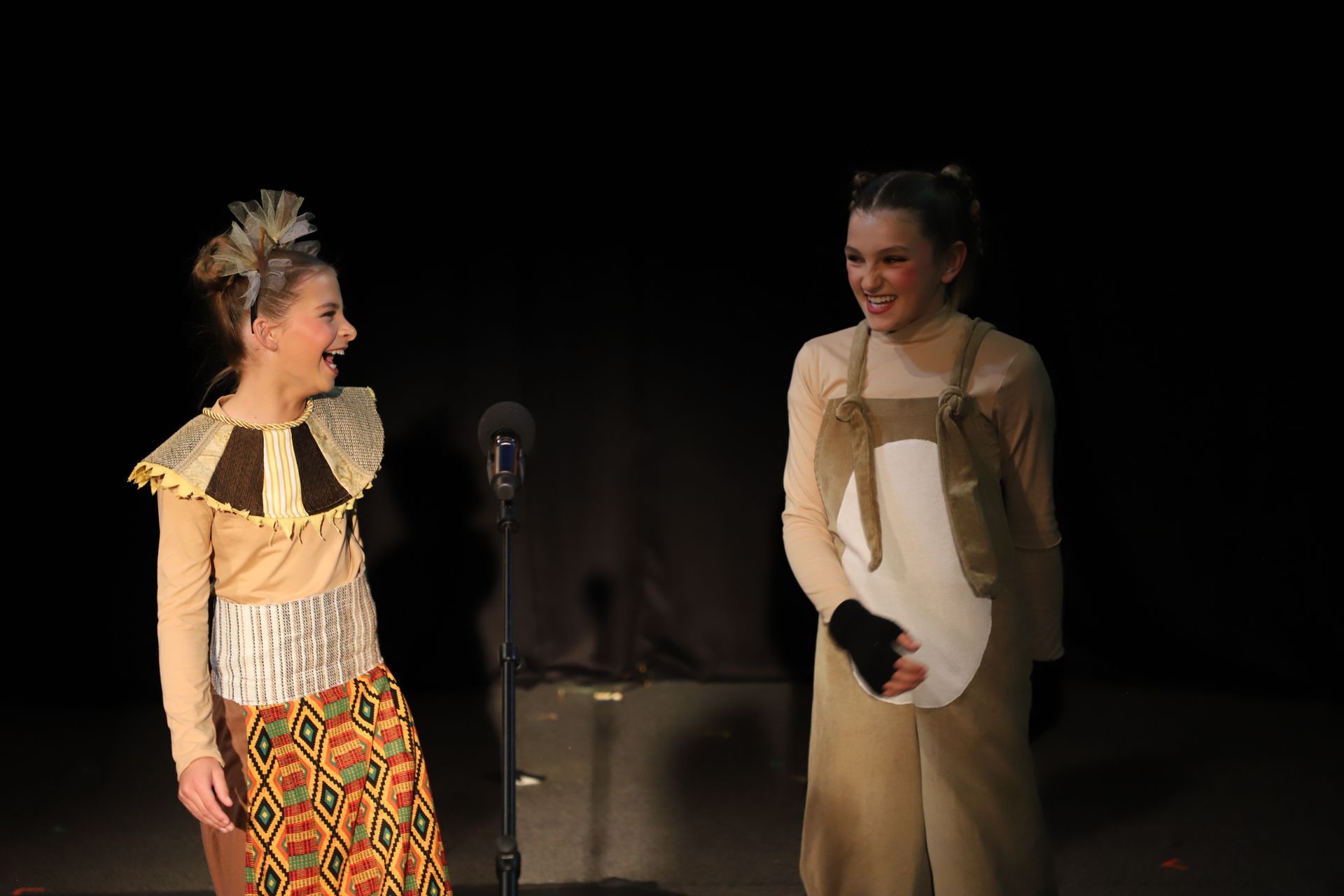 Two young girls are standing next to each other on a stage and laughing.
