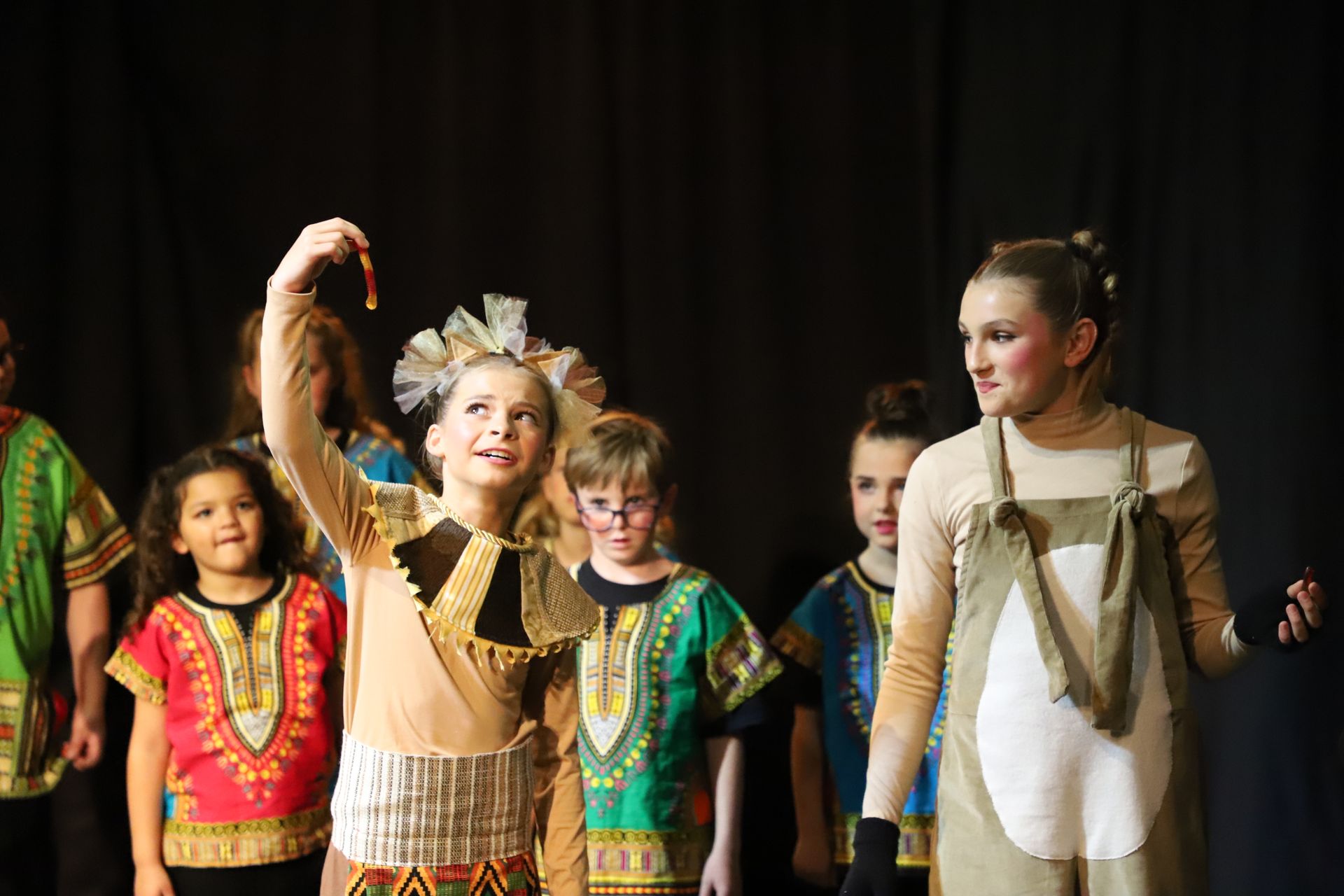 A group of children dressed in costumes are standing on a stage.