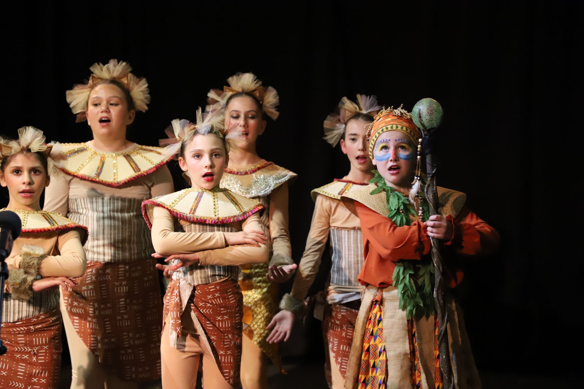 A group of children dressed in costumes are singing on a stage.