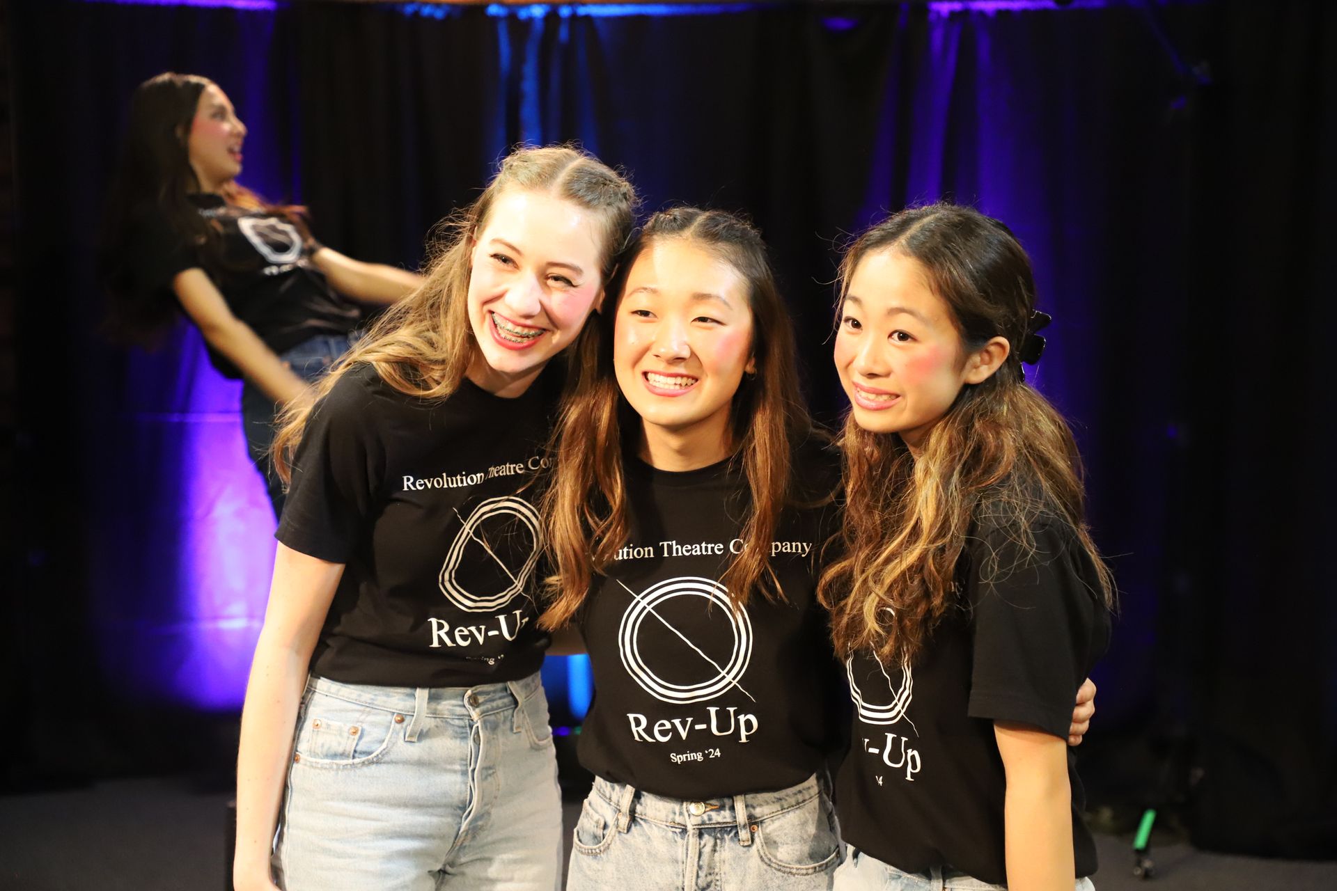 Three young women are posing for a picture in front of a purple curtain.