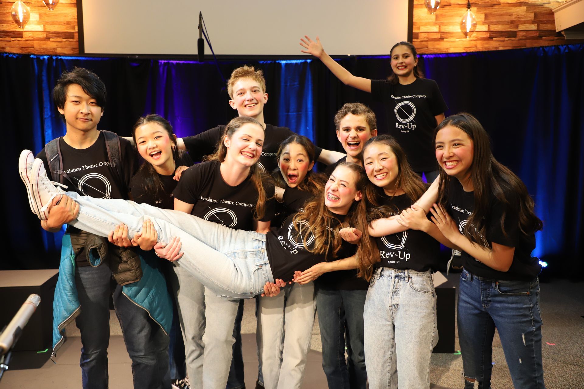 A group of young people are posing for a picture . one of the girls is holding another girl in her arms.