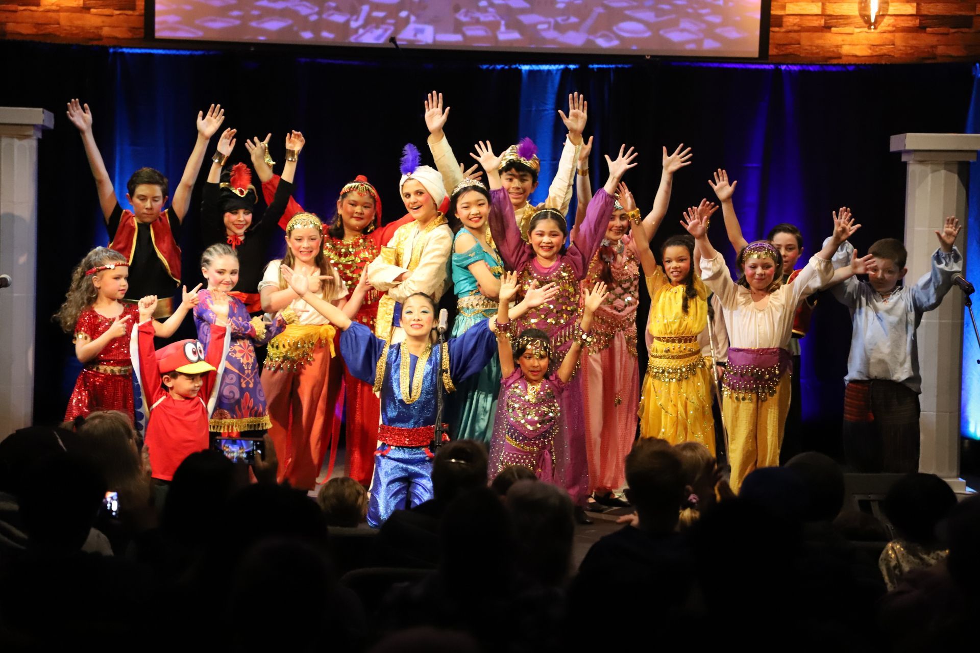 A group of children are standing on a stage with their hands in the air.