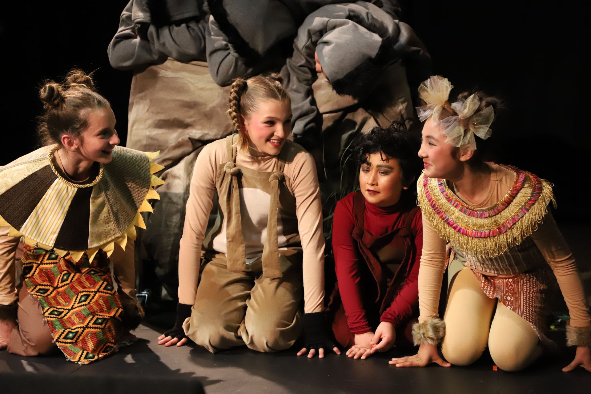 A group of people in costumes are sitting on the floor on a stage.