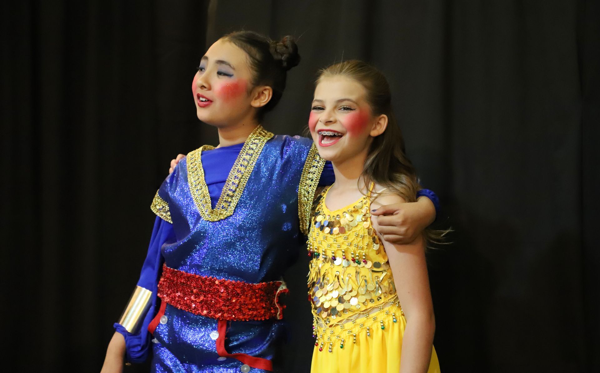 Two young girls are standing next to each other on a stage.
