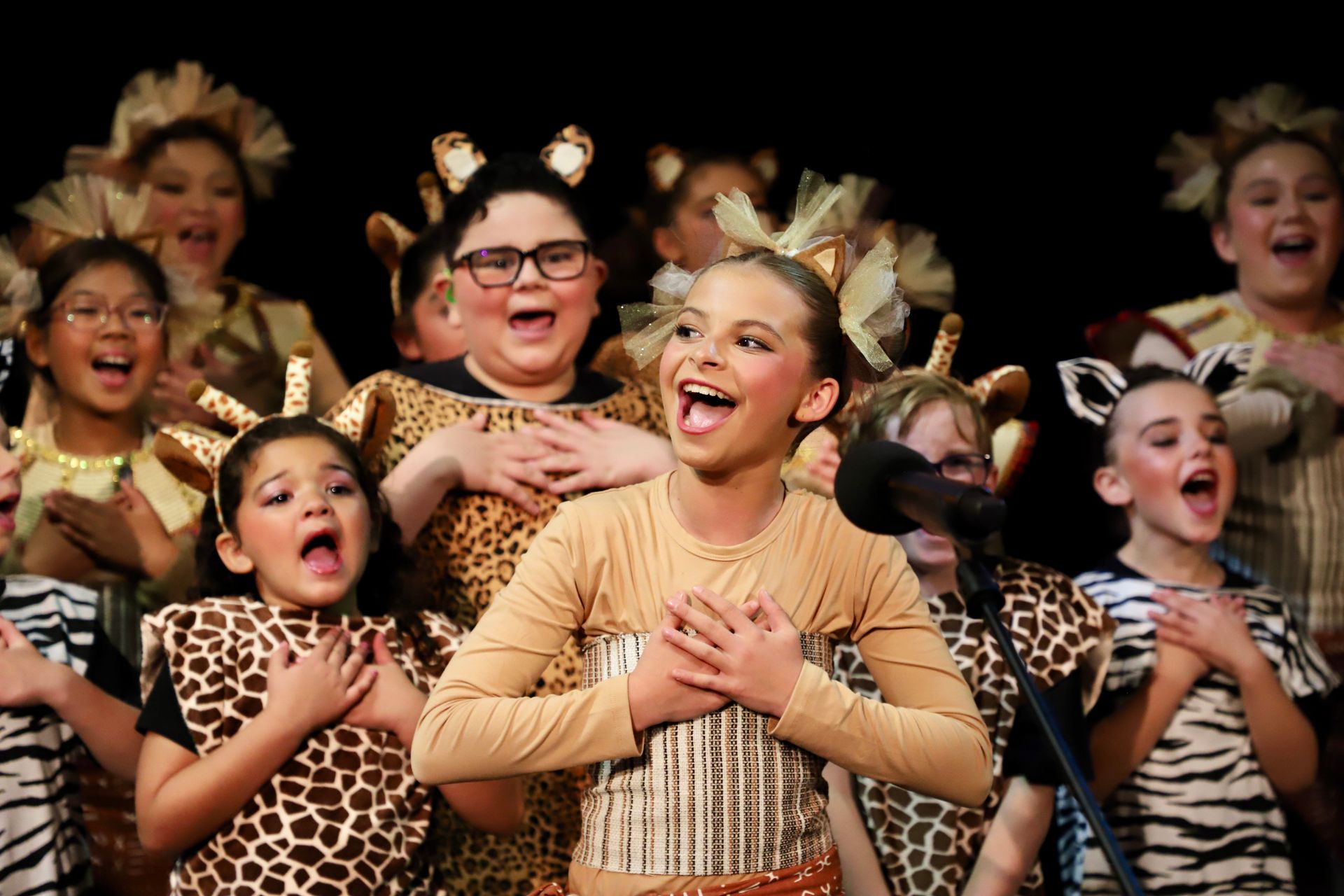 A group of children dressed in animal costumes are singing on a stage.