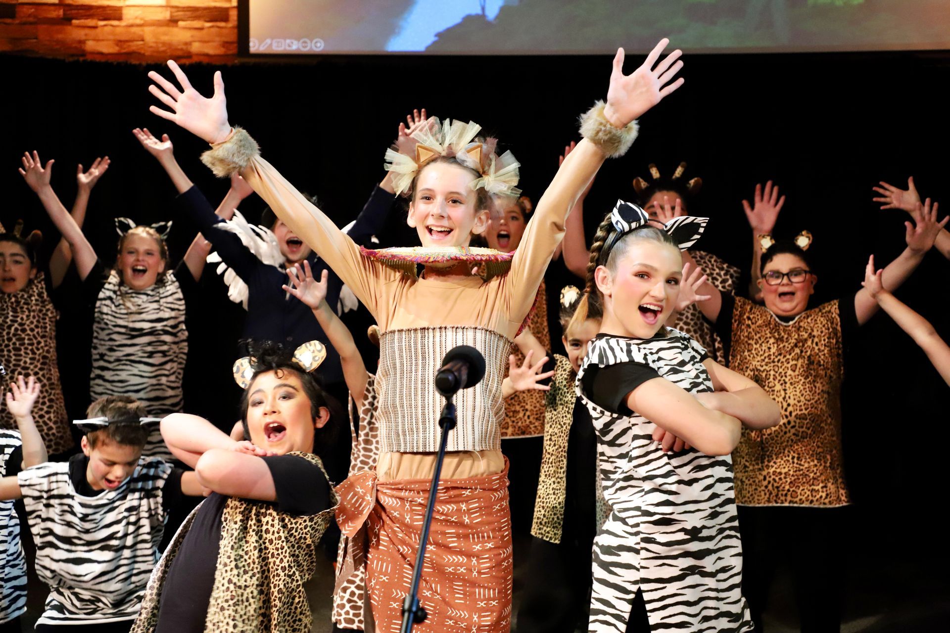 A group of children dressed in zebra print costumes are dancing in front of a microphone.