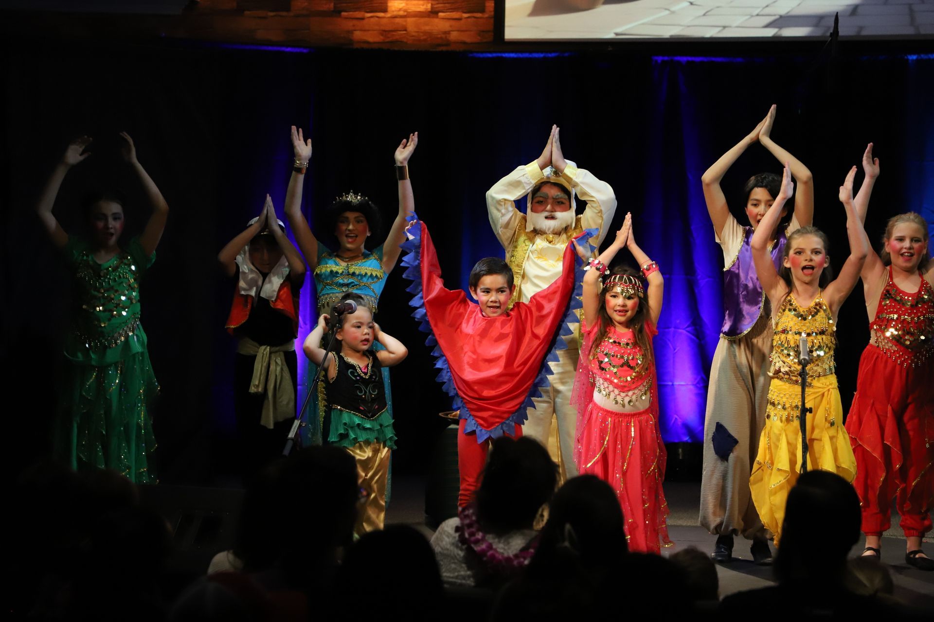 A group of children are dancing on a stage in front of a crowd.