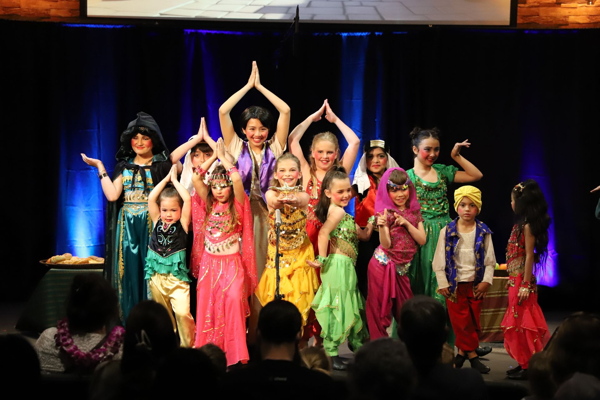 A group of children are dancing on a stage in front of a crowd.