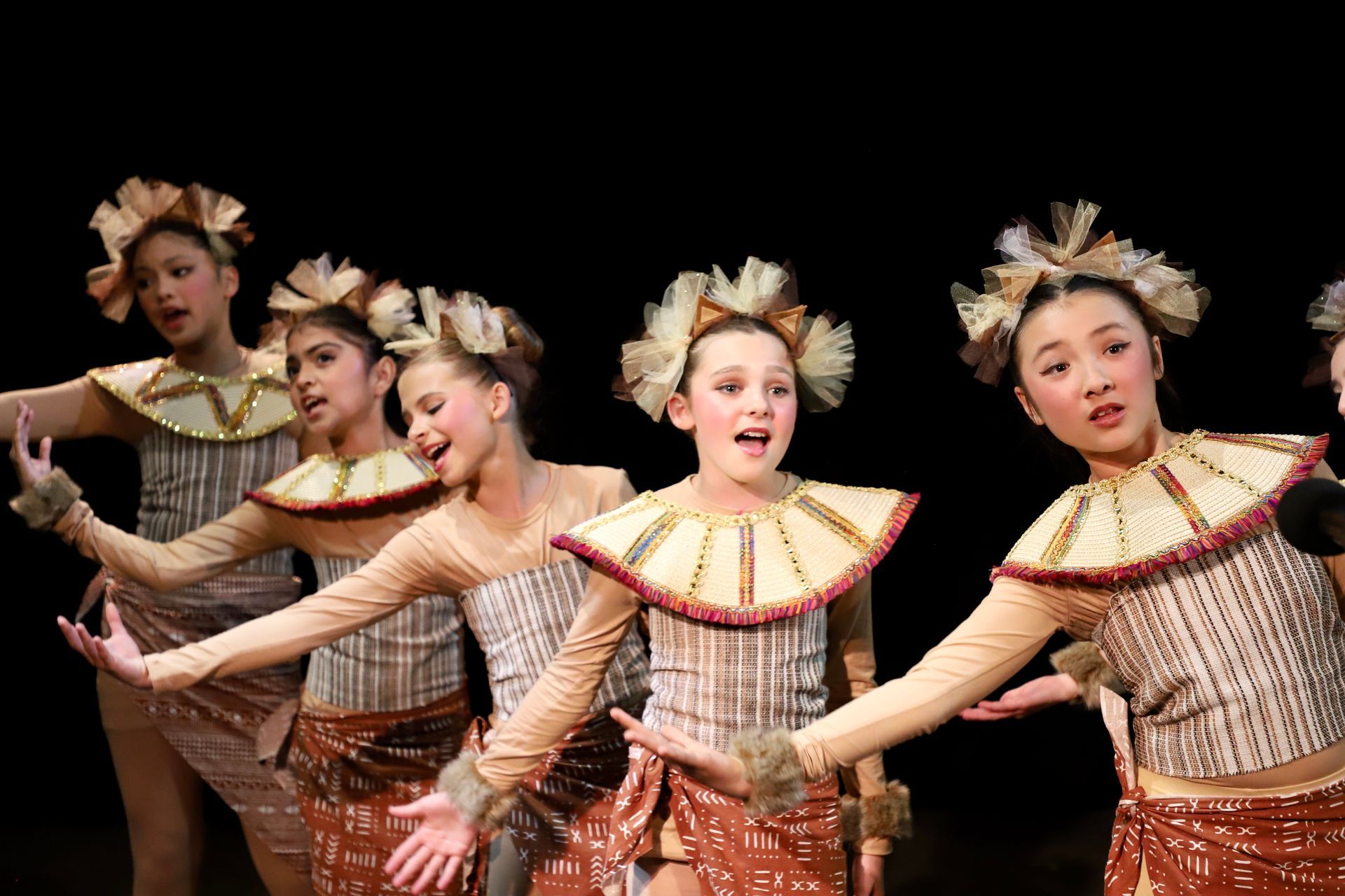 A group of young girls in costume are dancing on a stage.