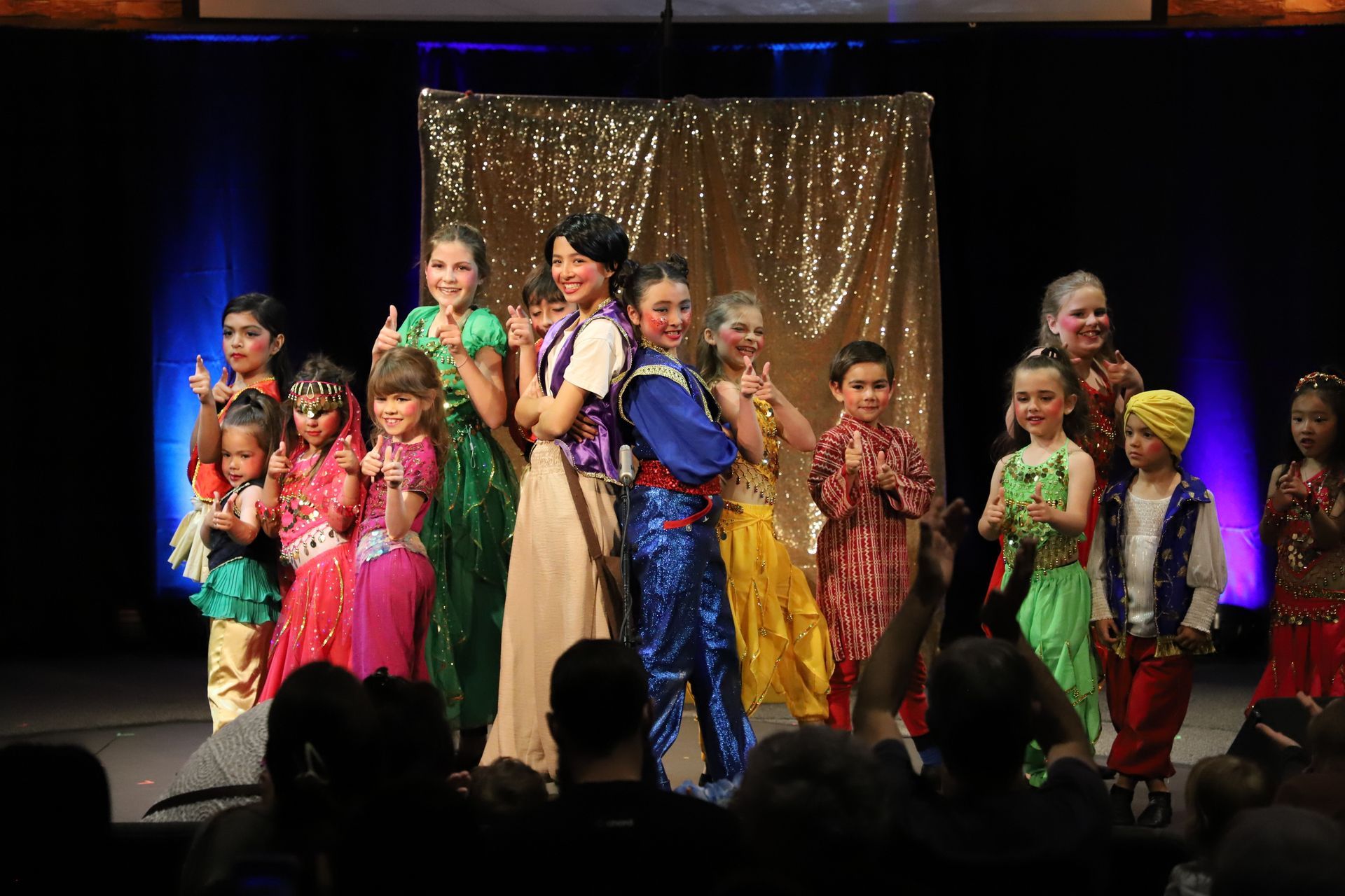 A group of children are dancing on a stage in front of a crowd.