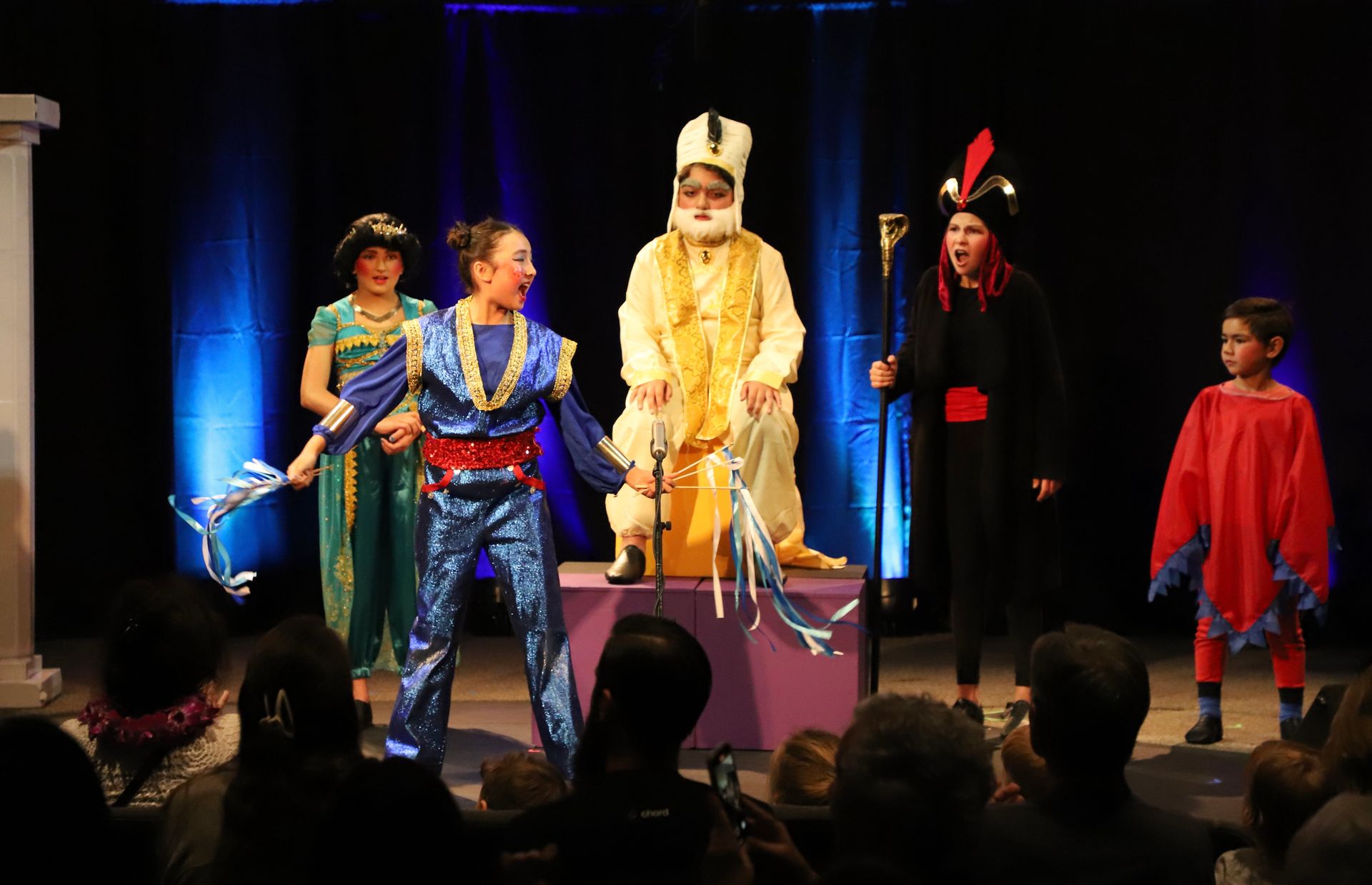 A group of people in costumes are standing on a stage in front of a crowd.