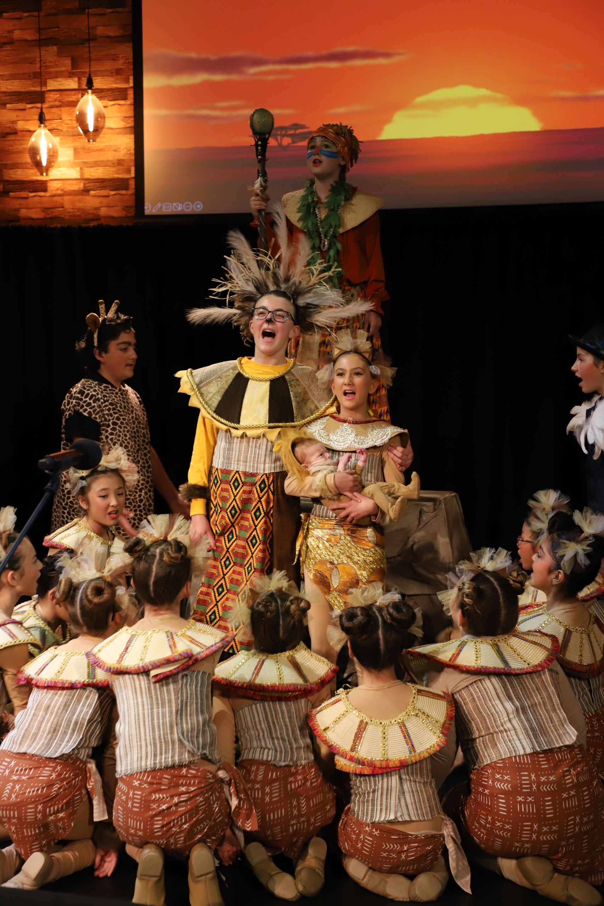 A group of people are kneeling down in front of a screen with a sunset in the background.