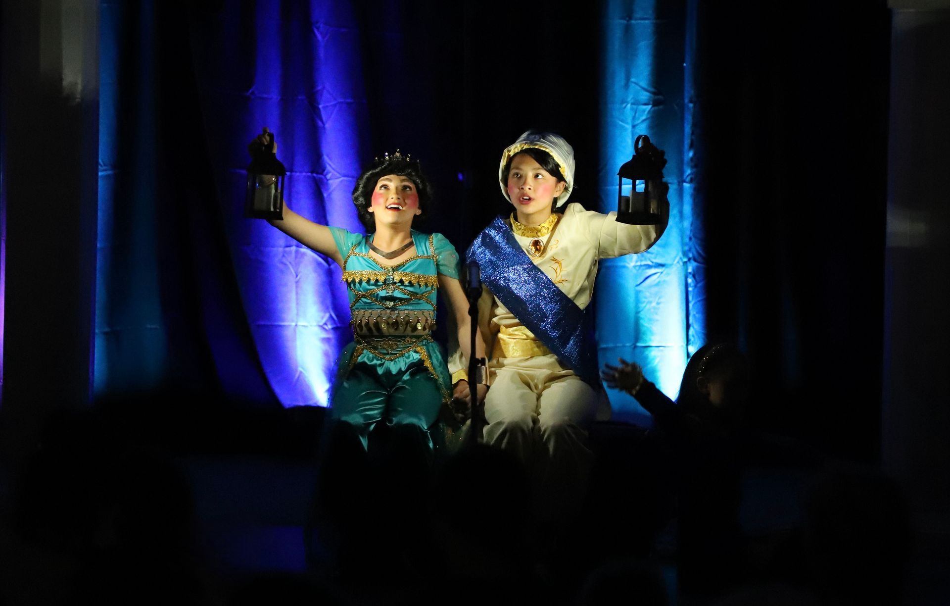 A boy and a girl are standing on a stage holding lanterns.