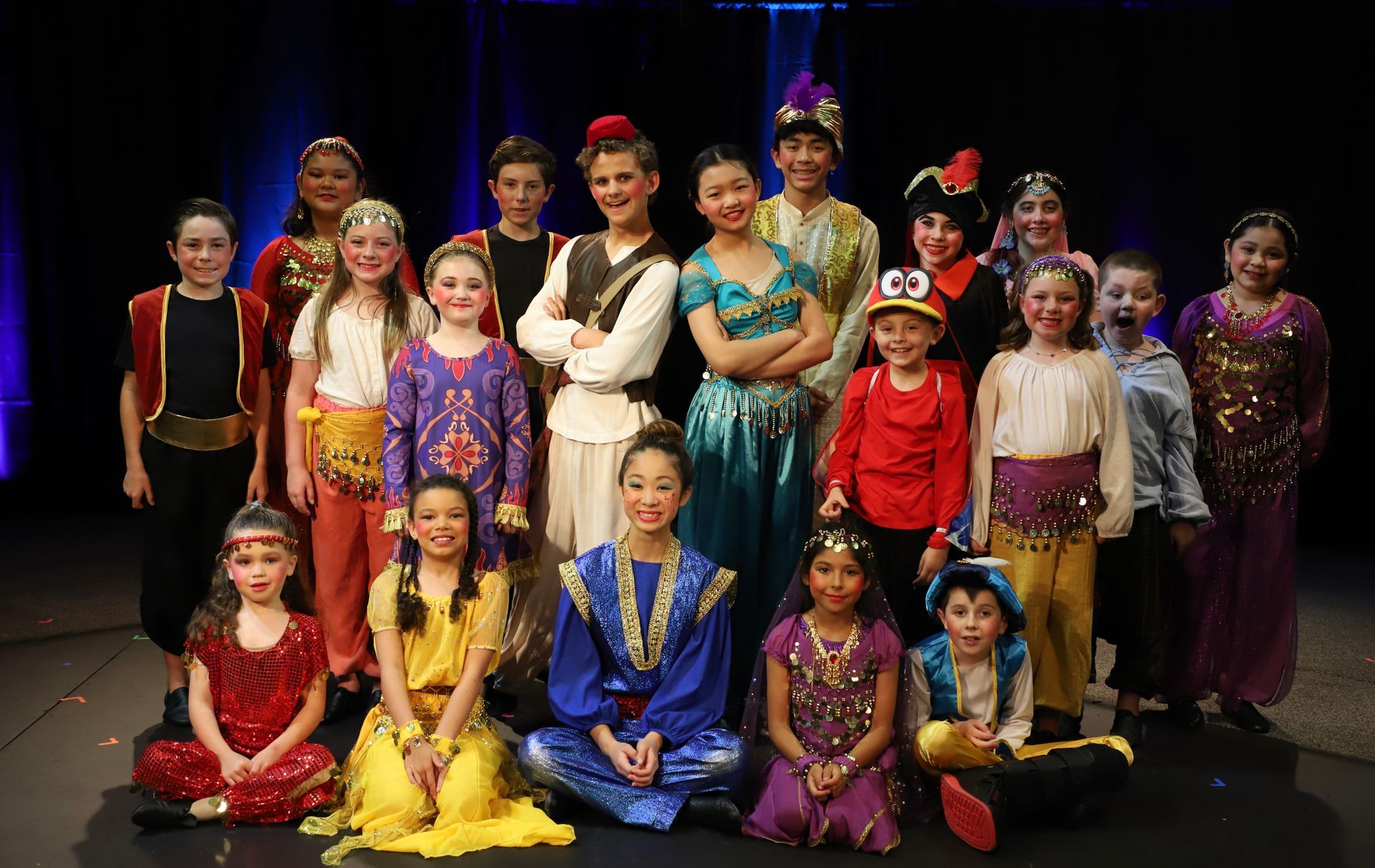 A group of children dressed in costumes are posing for a picture on a stage.