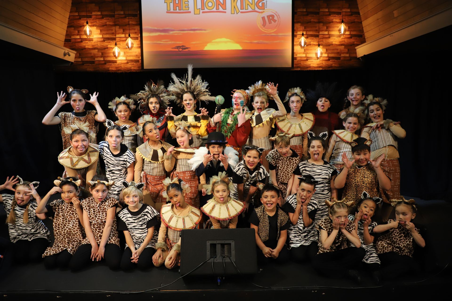 A group of children are posing for a picture in front of a screen that says the lion king
