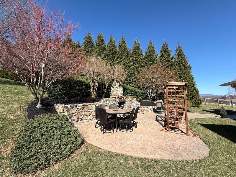 Backyard patio with outdoor dining set, stone fire pit, and pergola on a sunny day