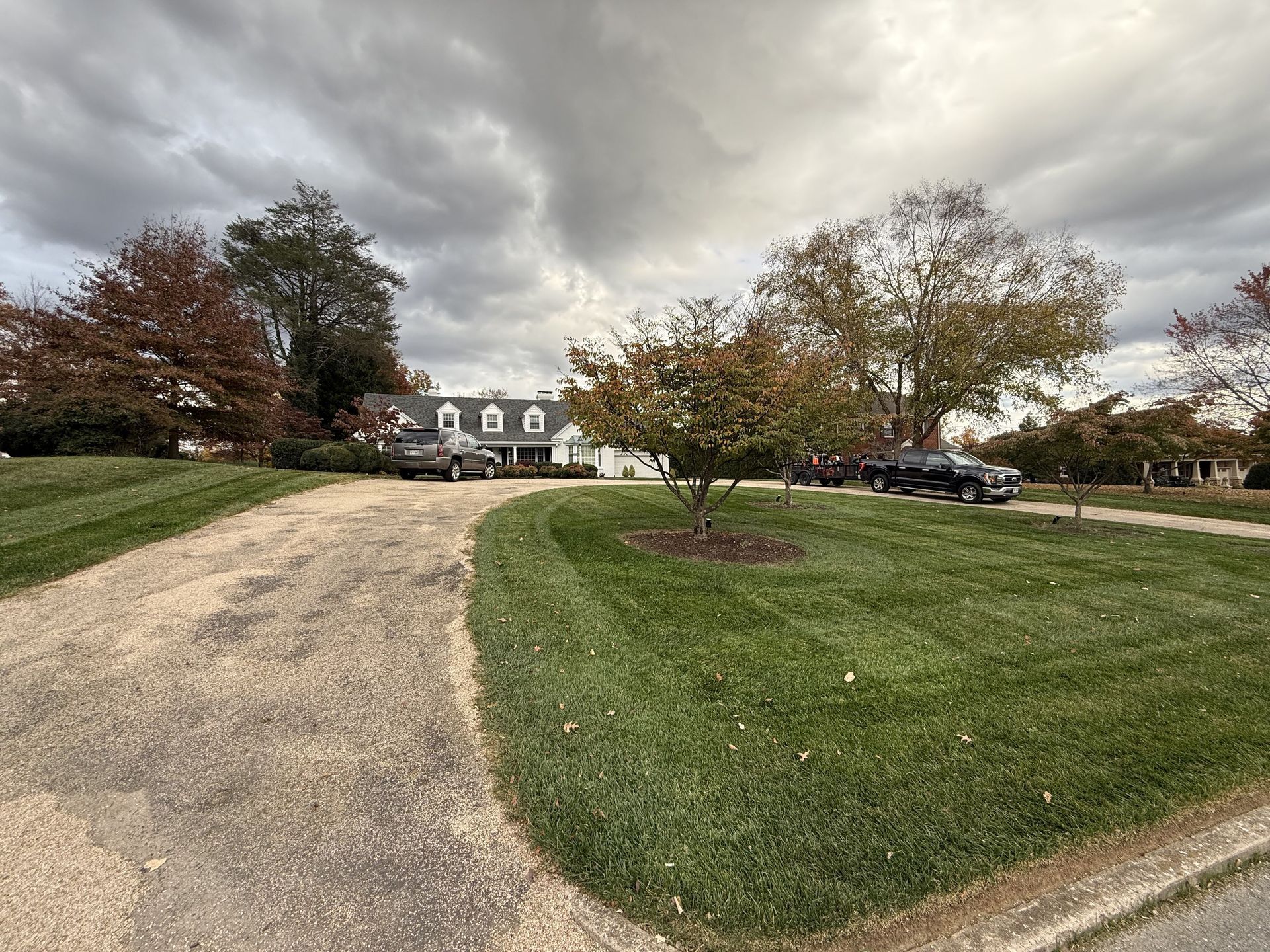 Curved driveway leading to a house with parked cars under a cloudy sky in a suburban yard