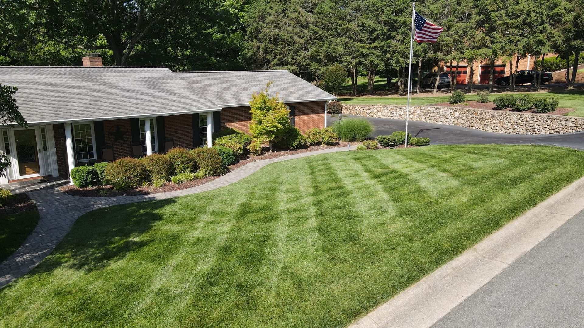 Suburban home with neatly striped lawn, landscaped garden, and an American flag by the road