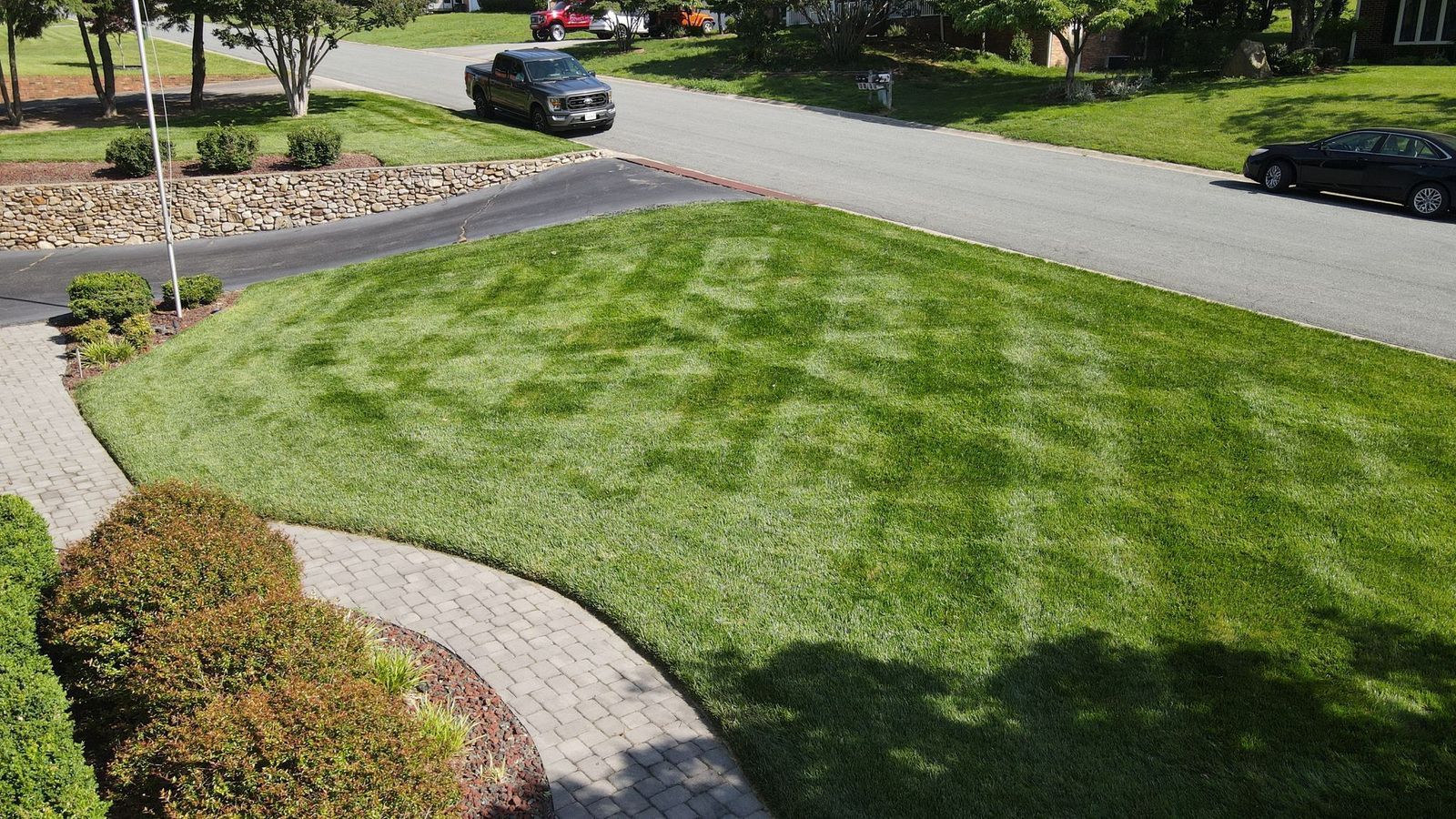 Landscaped front yard with green lawn, curved flower beds, and cars on a residential street