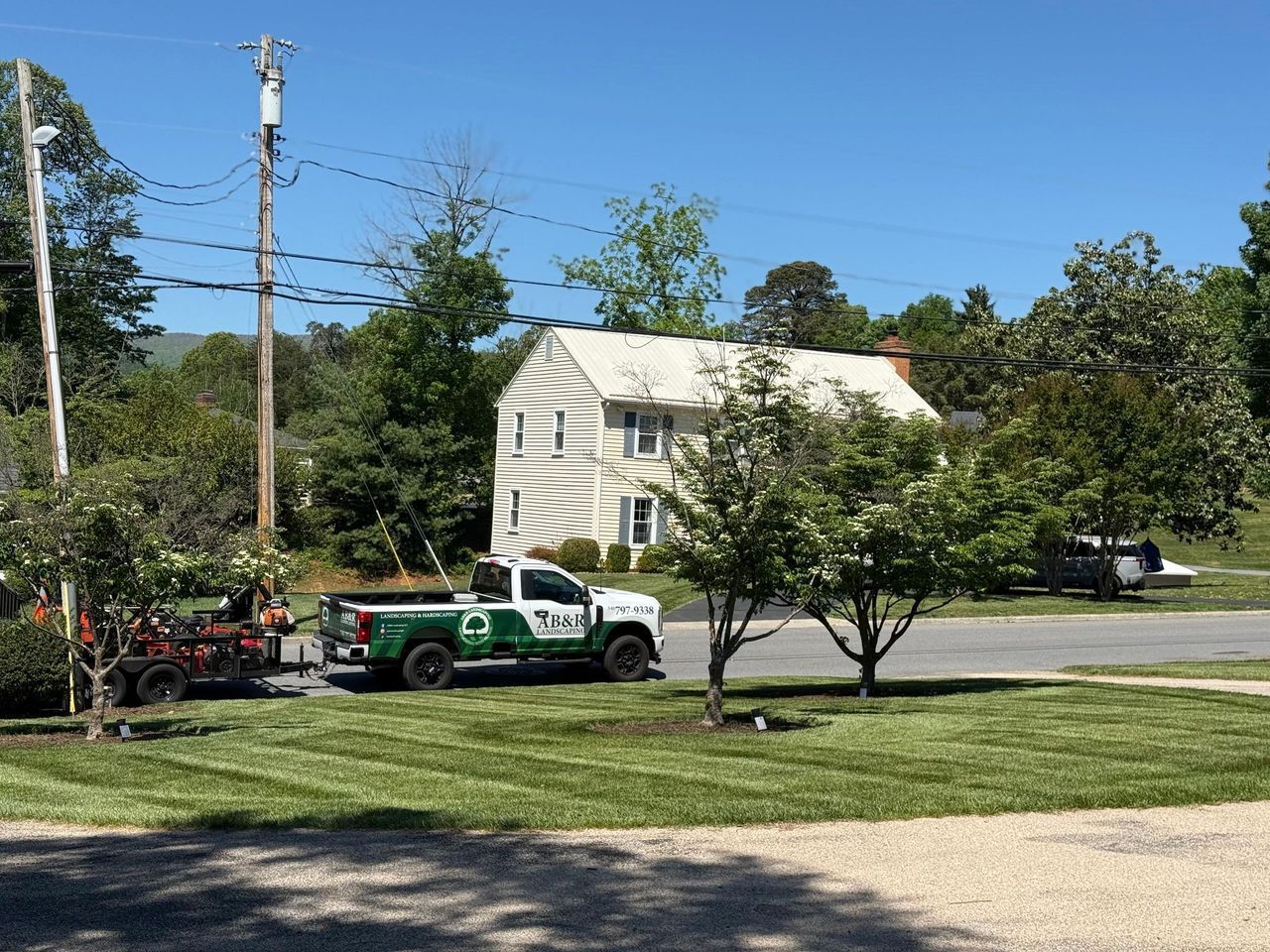 Green utility truck parked by a white house on a sunny suburban street.