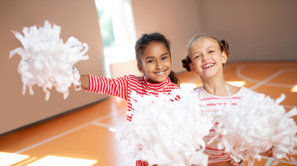 Two young girls are cheering with pom poms in a gym.