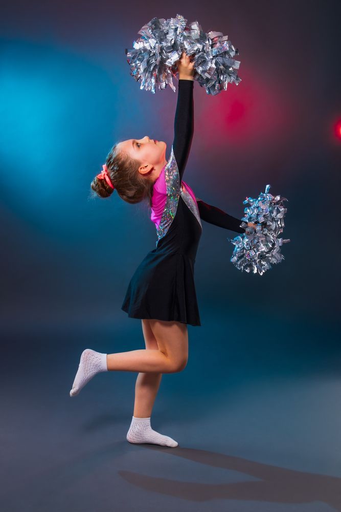 A young girl in a cheerleading uniform is holding pom poms in the air.