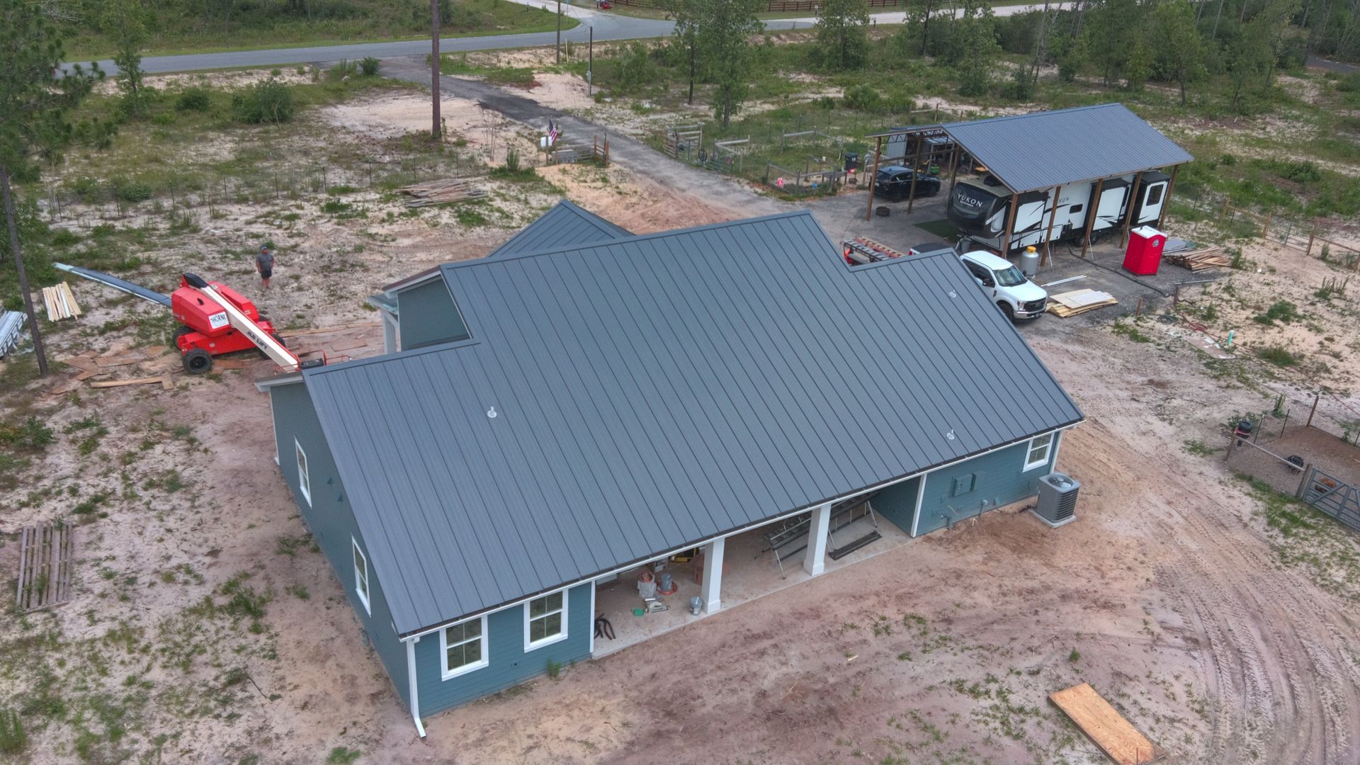 Aerial view of a blue house under construction with a dark gray roof.  A detached building is beside it.