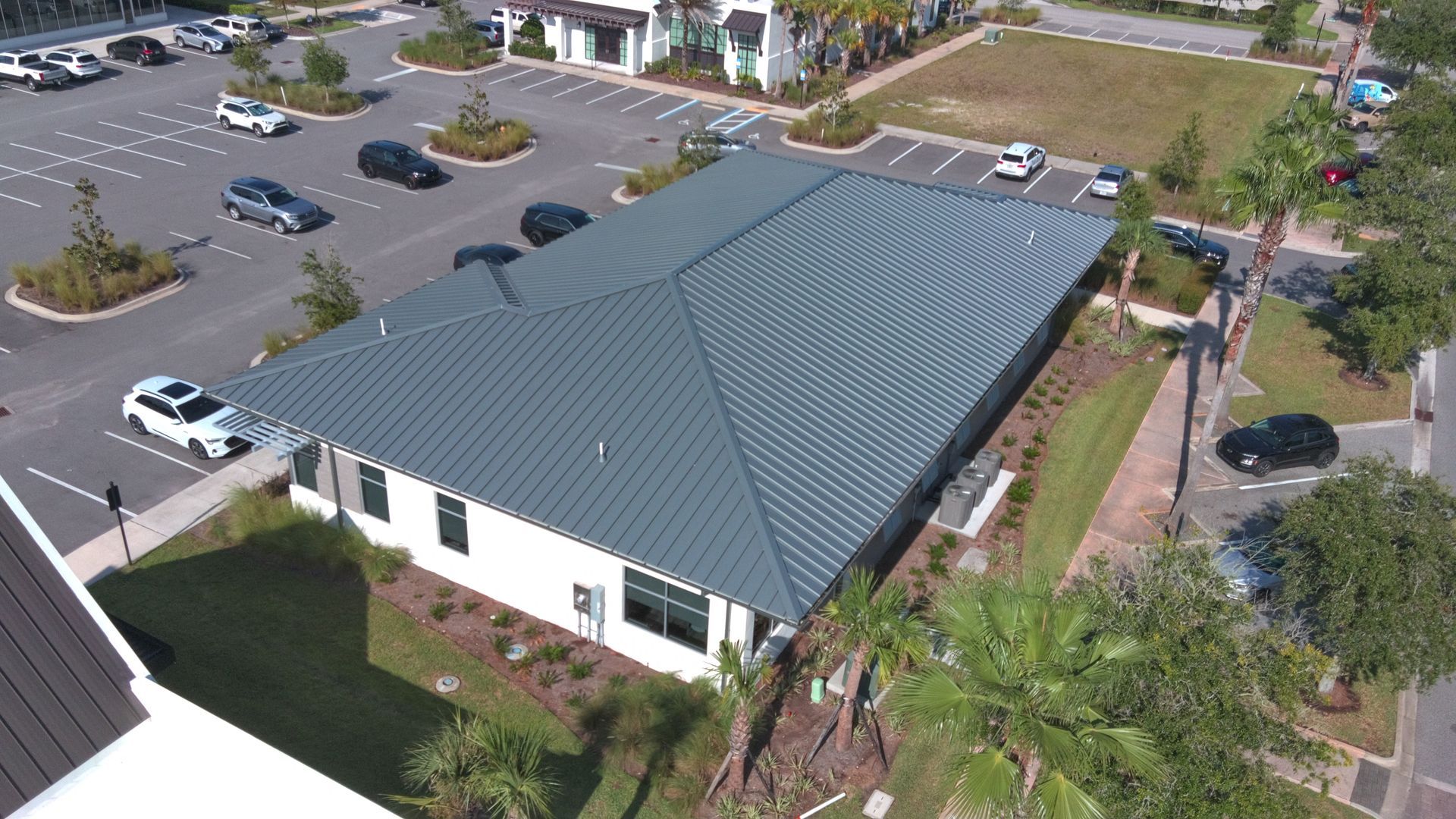 Aerial view of a gray-roofed building with surrounding parking lot and greenery.