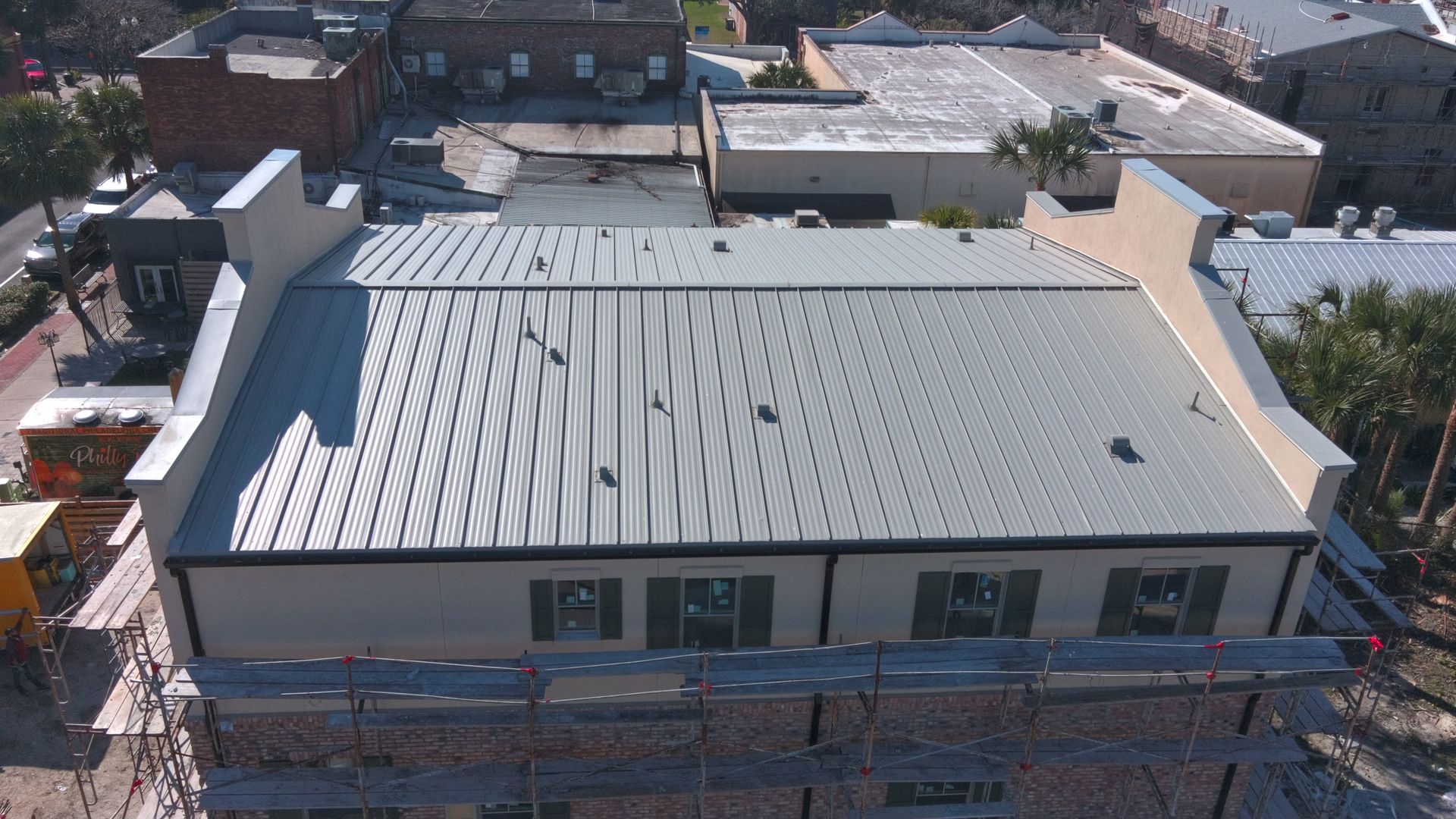 Aerial view of a building with a metal roof, scaffolding, and surrounding buildings.